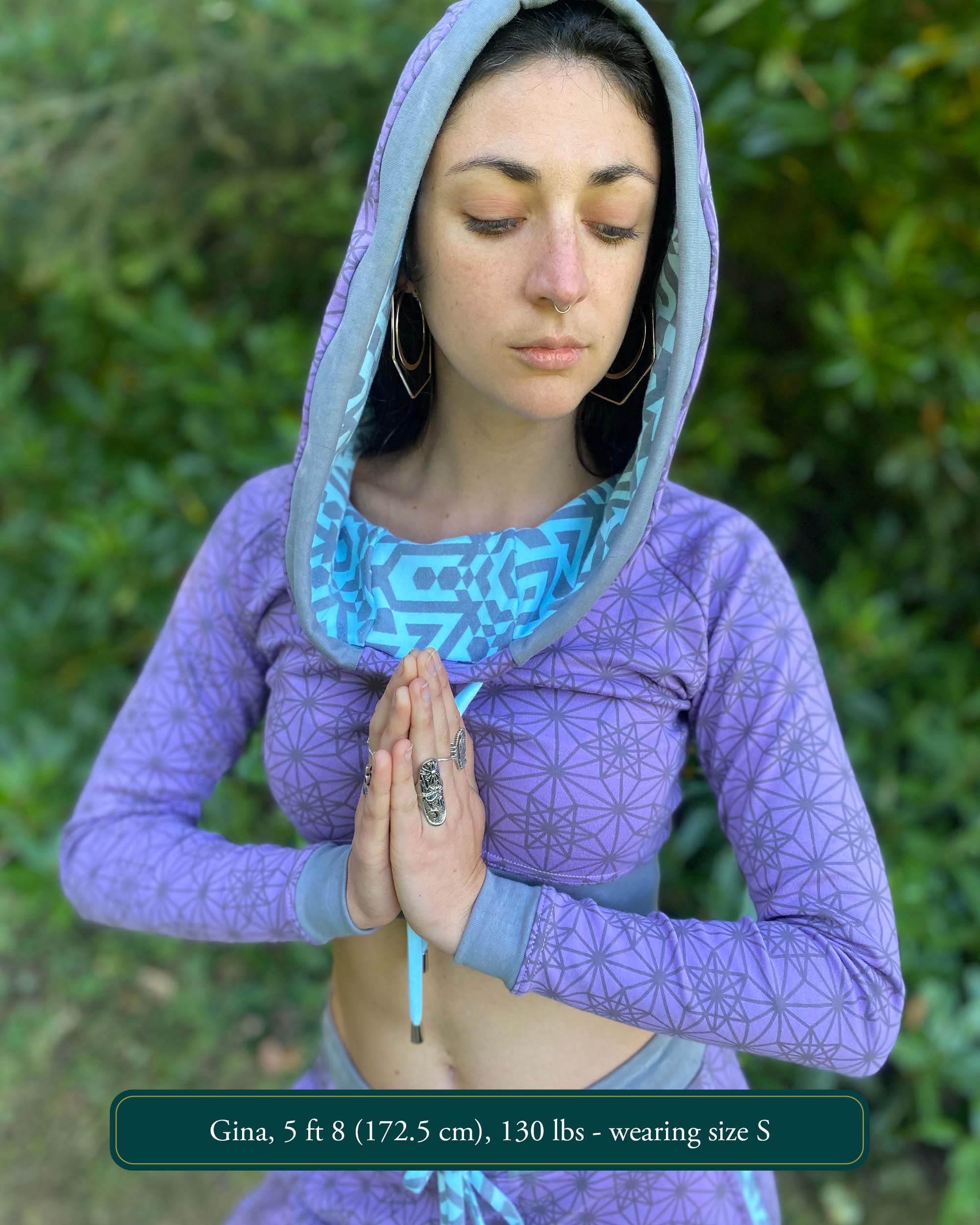 A woman wearing an organic cotton lavender crop hoodie with geometric print, worn with hood up, front view.