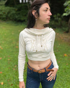 A woman wearing an organic cotton undyed crop hoodie with a gold print, cowl hood and long sleeves, right side view.