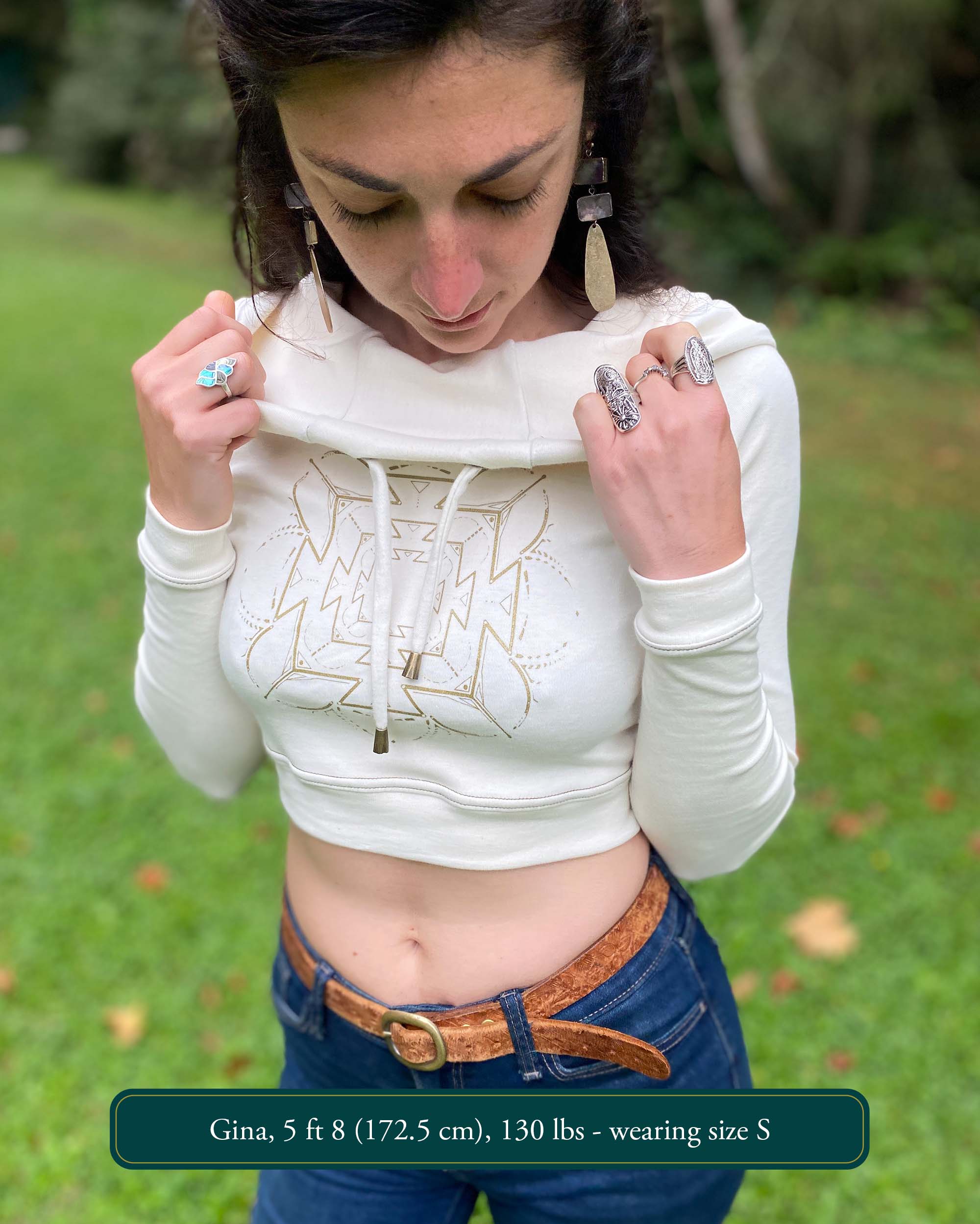A woman wearing an organic cotton undyed crop hoodie with a gold print, cowl hood and long sleeves, front view.