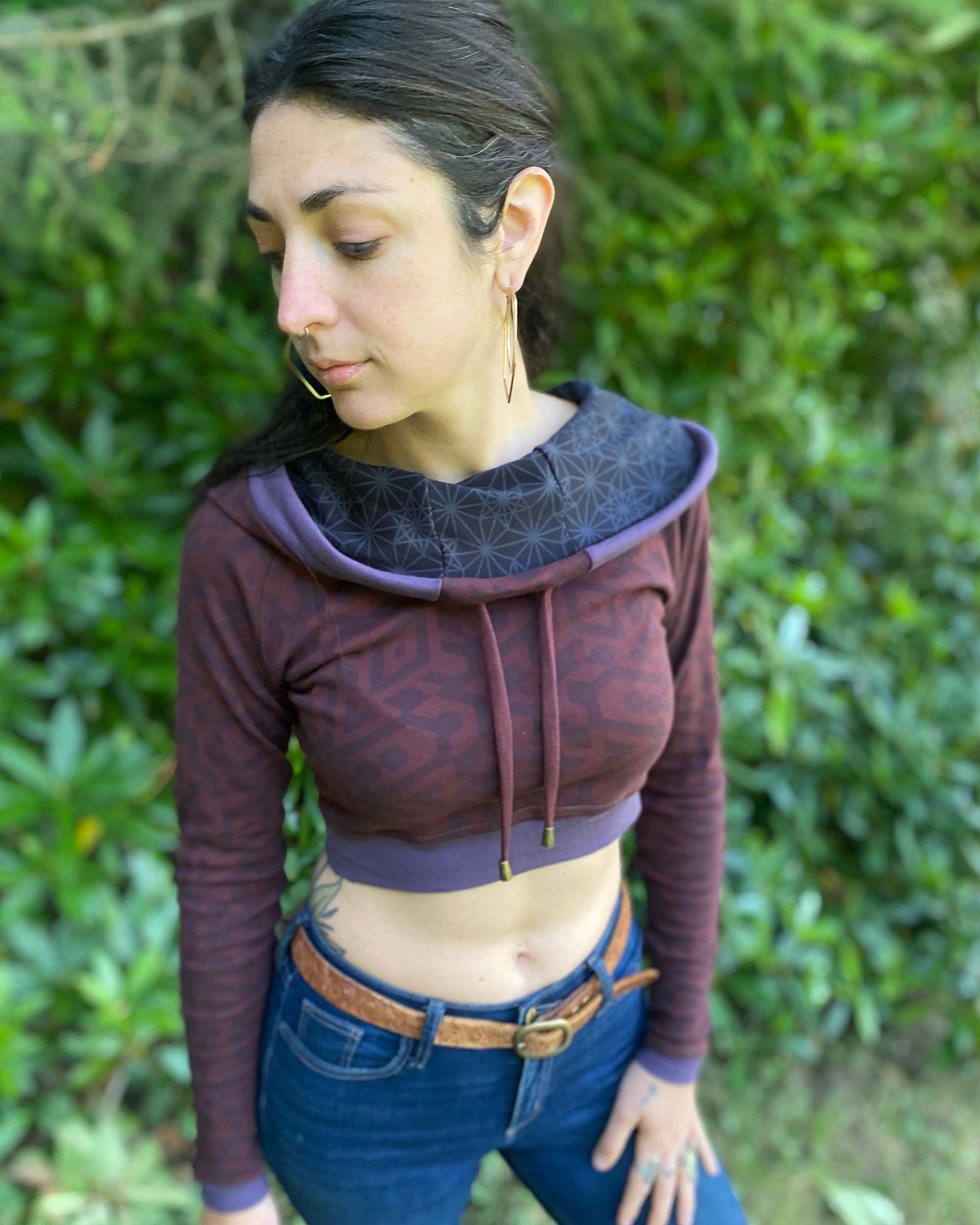 A woman wearing an organic cotton brown crop hoodie with geometric print and purple accents, front left view.