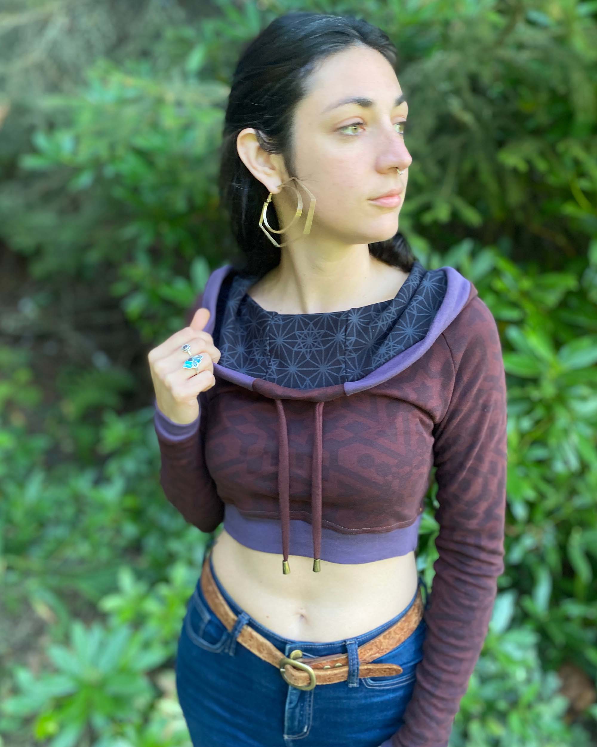 A woman wearing an organic cotton brown crop hoodie with geometric print and purple accents, front view.