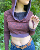 A woman wearing an organic cotton brown crop hoodie with geometric print and purple accents, detail view of antique brass drawcord ends.
