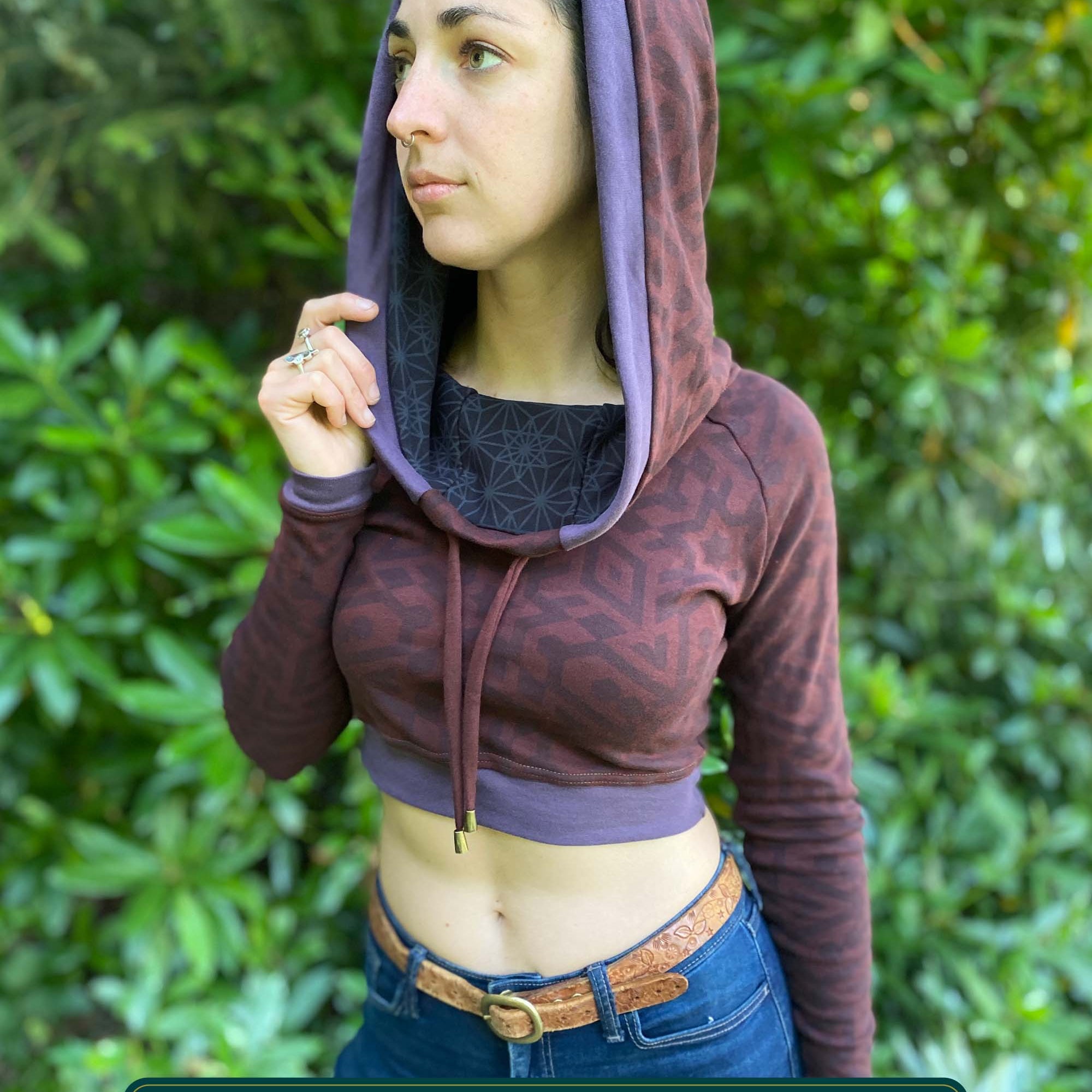 A woman wearing an organic cotton brown crop hoodie with geometric print and purple accents, front side view.