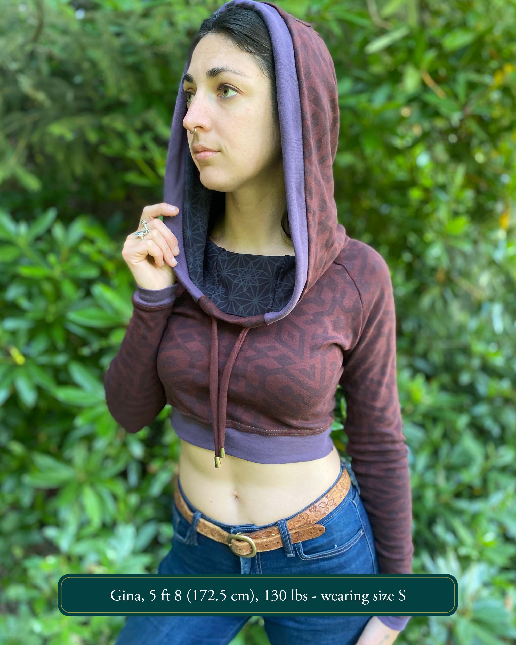 A woman wearing an organic cotton brown crop hoodie with geometric print and purple accents, front side view.