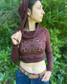 A woman wearing an organic cotton reddish brown crop hoodie with a gold print, cowl hood and long sleeves, right side front view.
