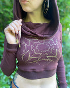 A woman wearing an organic cotton reddish brown crop hoodie with a gold print, cowl hood and long sleeves, detail front view.