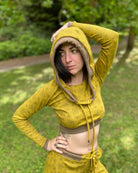 A woman wearing an organic cotton yellow crop hoodie with geometric print, cowl neck and long sleeves, worn with hood up.