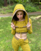 A woman wearing an organic cotton yellow crop hoodie with geometric print, cowl neck and long sleeves, front view in a outdoor setting.