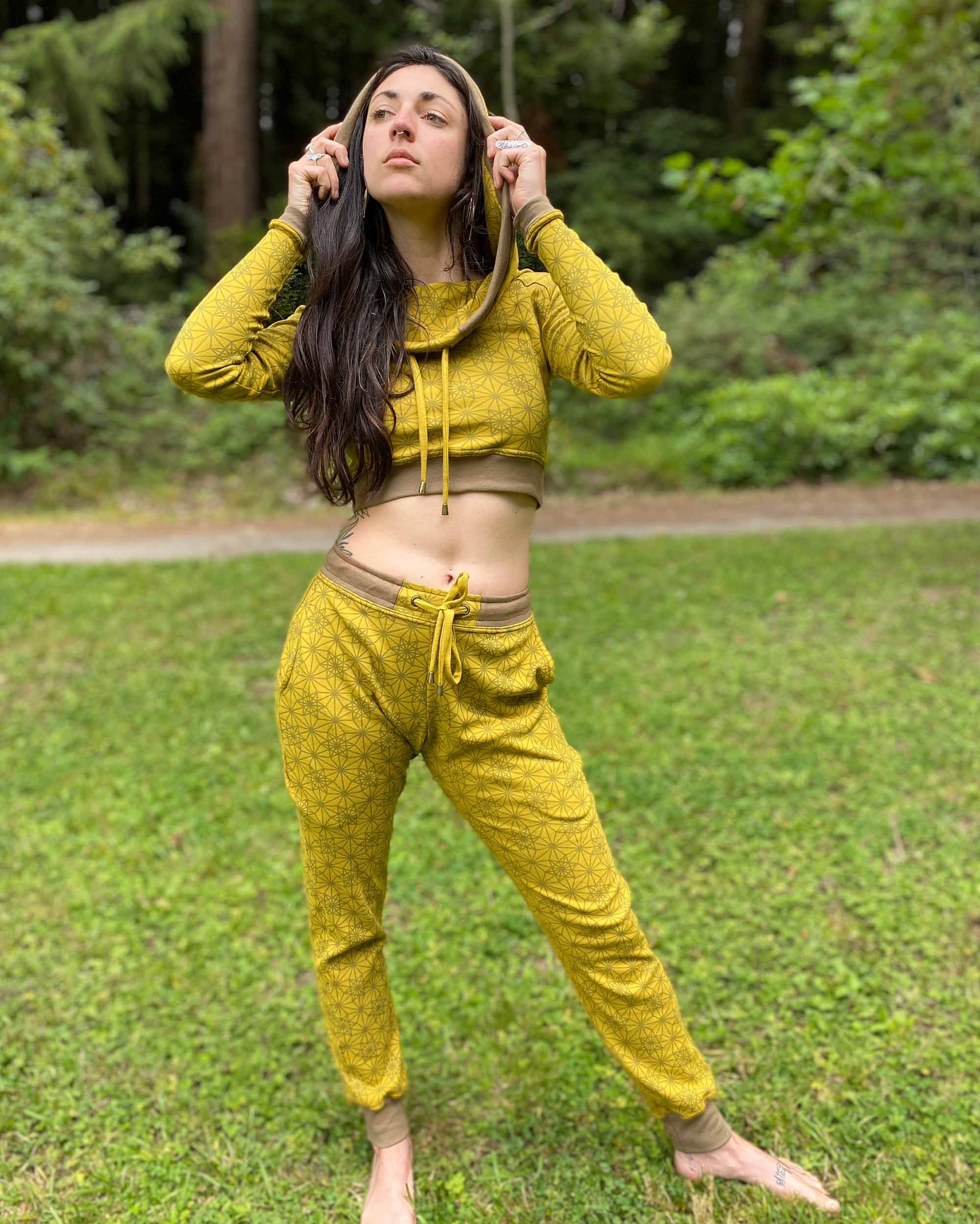 A woman wearing an organic cotton yellow crop hoodie with geometric print, with matching joggers, front view in a outdoor setting.
