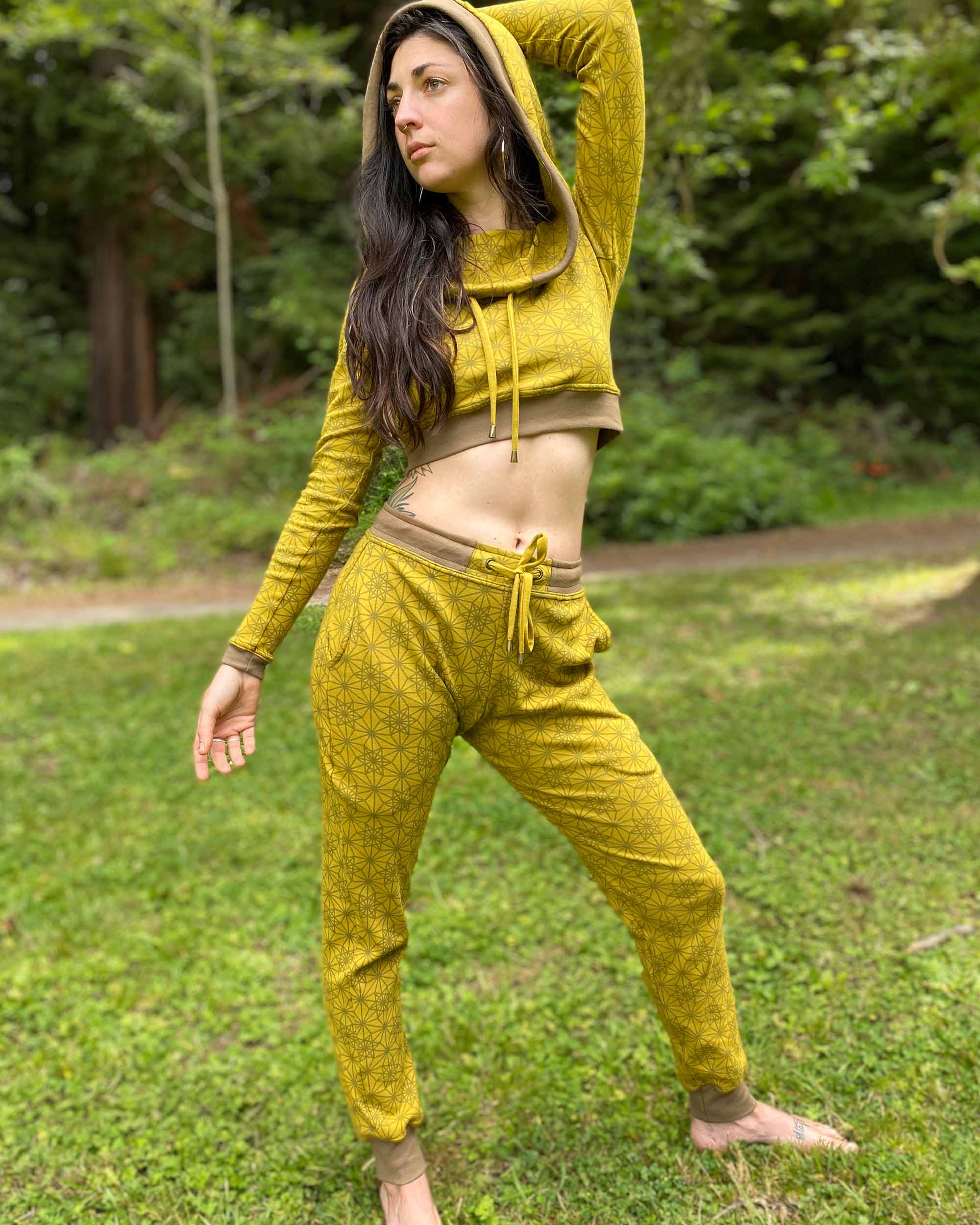 A woman wearing an organic cotton yellow crop hoodie with geometric print, with matching joggers, front view in nature.