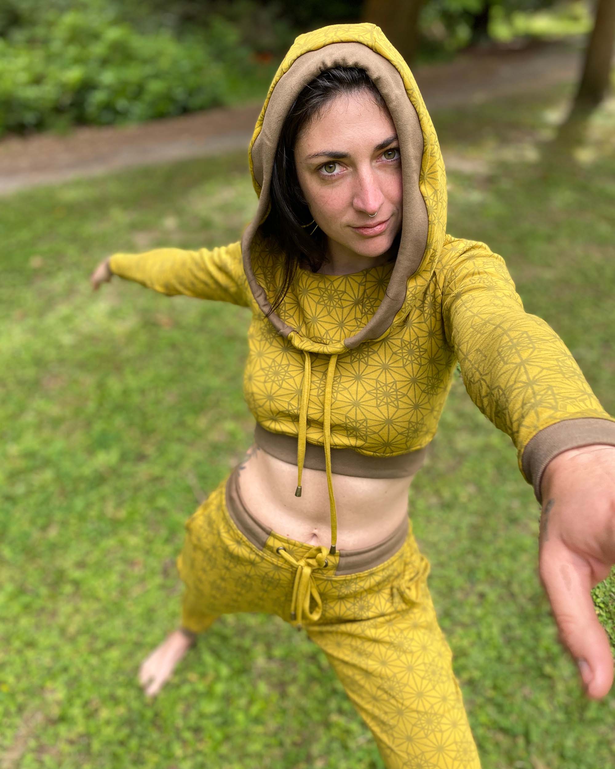 A woman doing yoga wearing an organic cotton yellow crop hoodie with geometric print, with matching joggers.