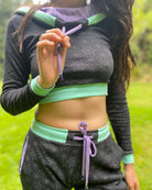 A woman wearing an organic cotton black crop hoodie with geometric print and purple accents, cowl hood and long sleeves, close up view of drawcord details.