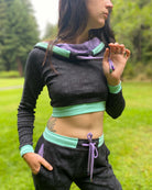 A woman wearing an organic cotton black crop hoodie with geometric print and purple accents, close up view of drawcord details.