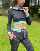 A woman wearing an organic cotton black crop hoodie with geometric fabric print and purple accents with matching joggers, front view.