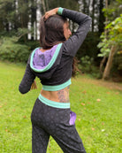 A woman wearing an organic cotton black crop hoodie with geometric print and purple accents with matching joggers, back view.