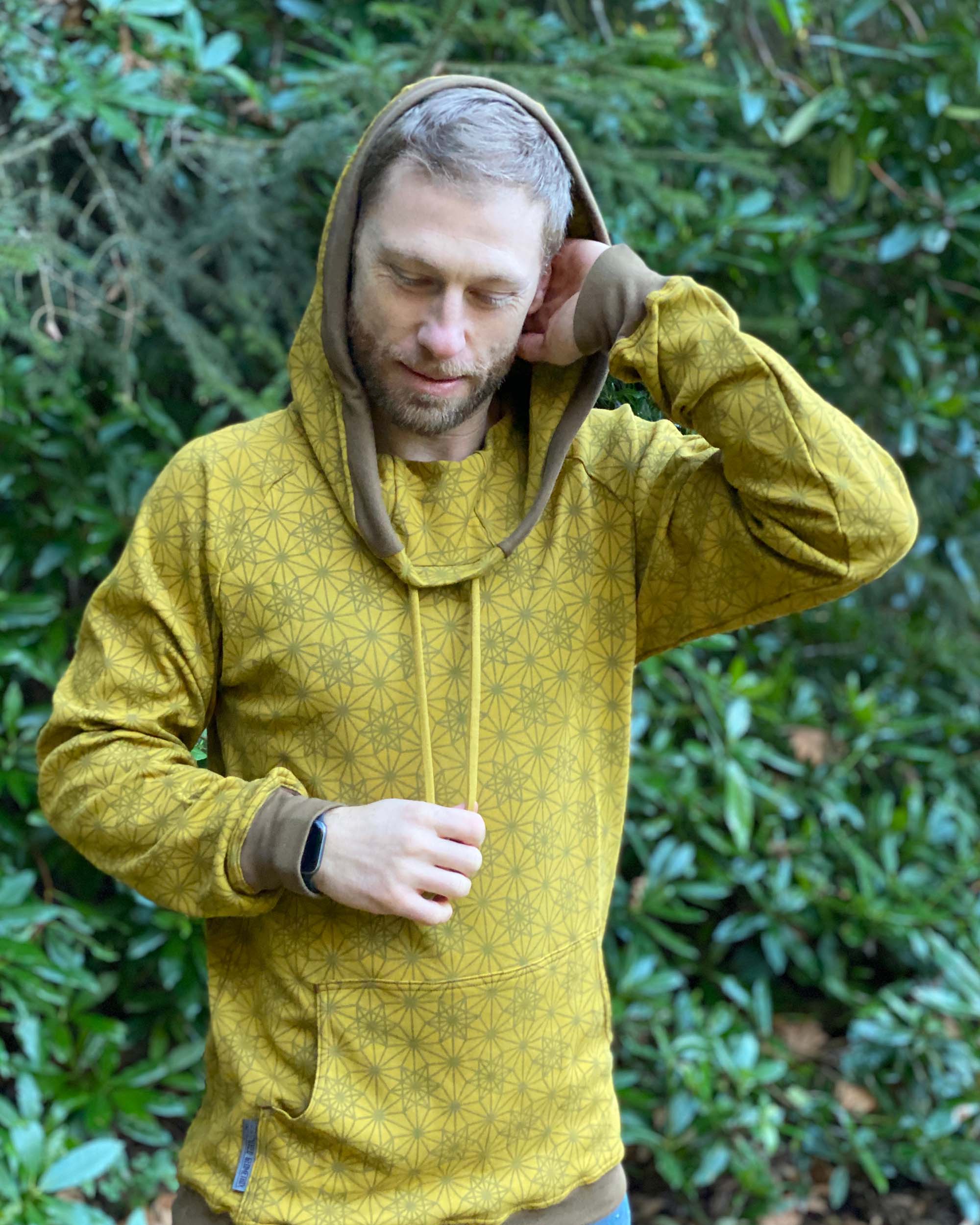 Organic cotton extra long unisex hoodie, yellow fabric with geometric print, front view of model in nature.