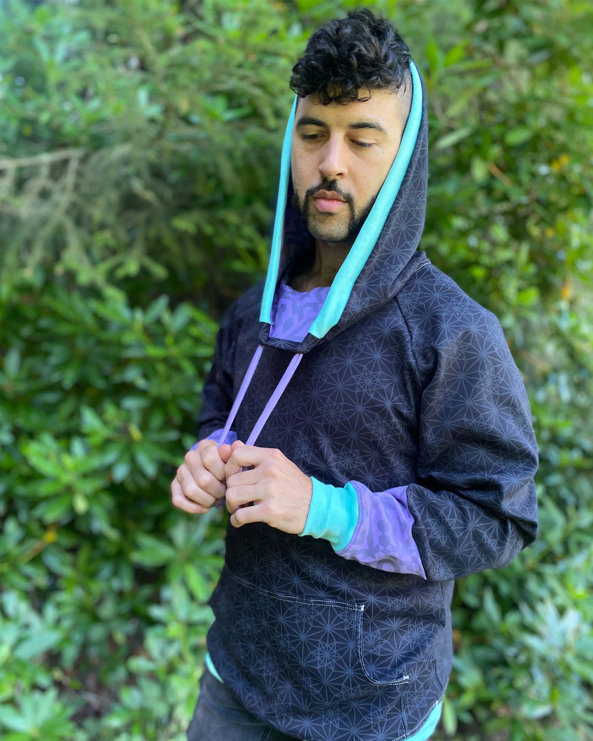 Organic cotton hoodie, black with sacred geometry print and lavender accents, side view on male model.