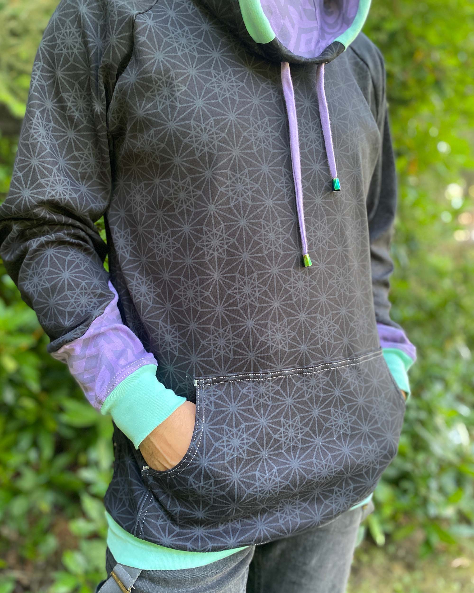 Organic cotton hoodie, black with sacred geometry print and lavender accents, detail view of fabric.