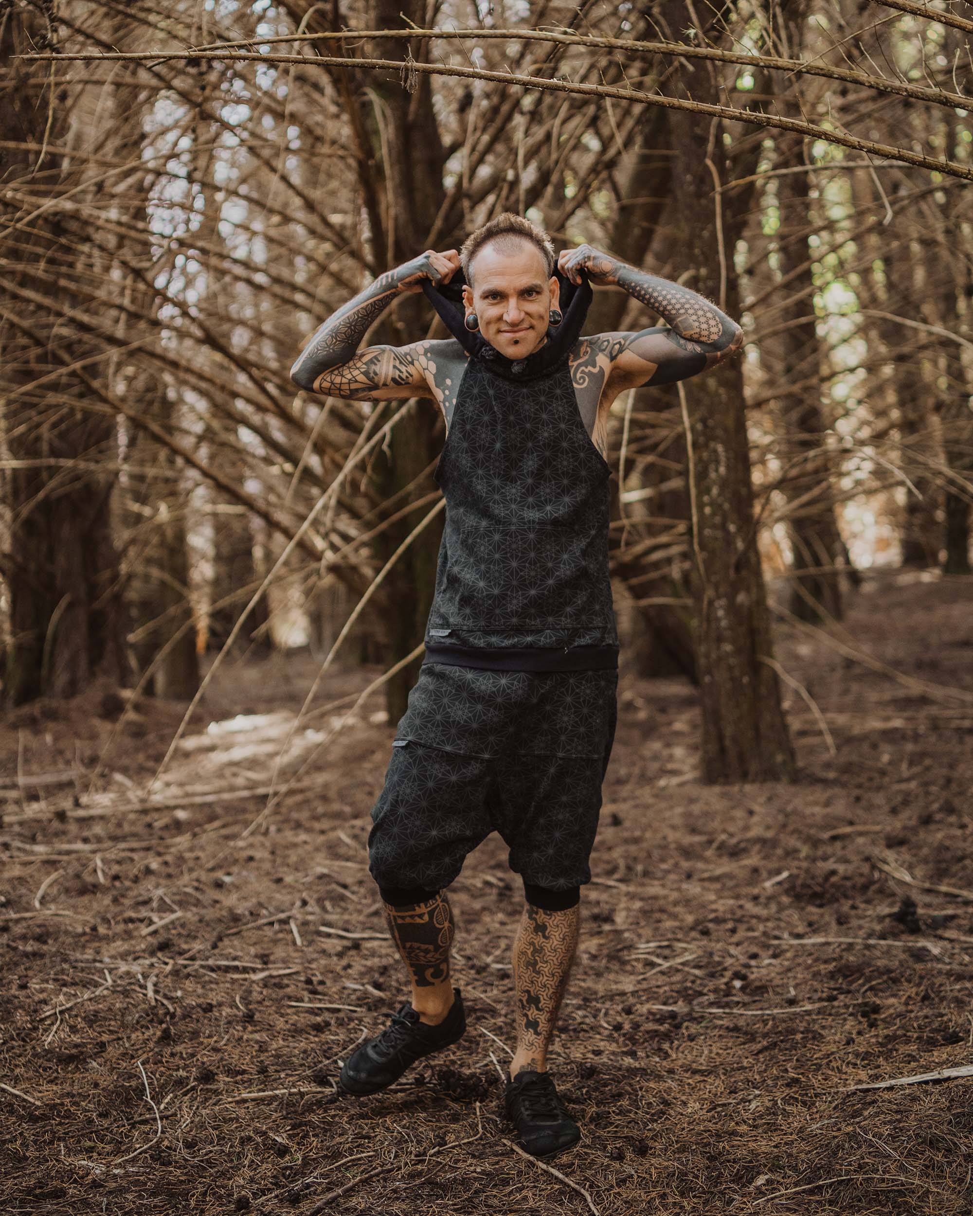 Organic cotton sleeveless hoodie, black with sacred geometry print, front view on male model in nature.