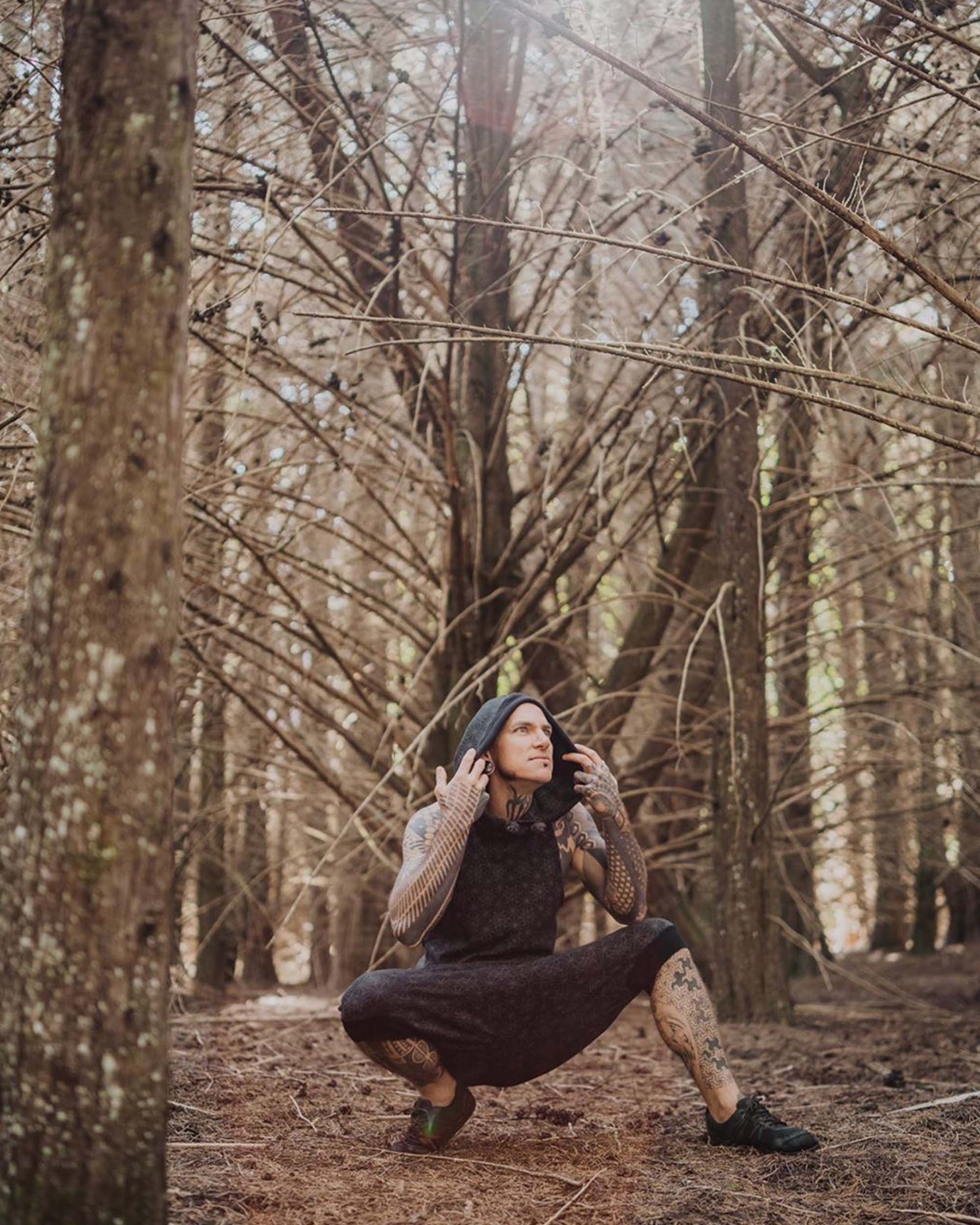Organic cotton sleeveless hoodie, black with sacred geometry print, front view on male model crouching.