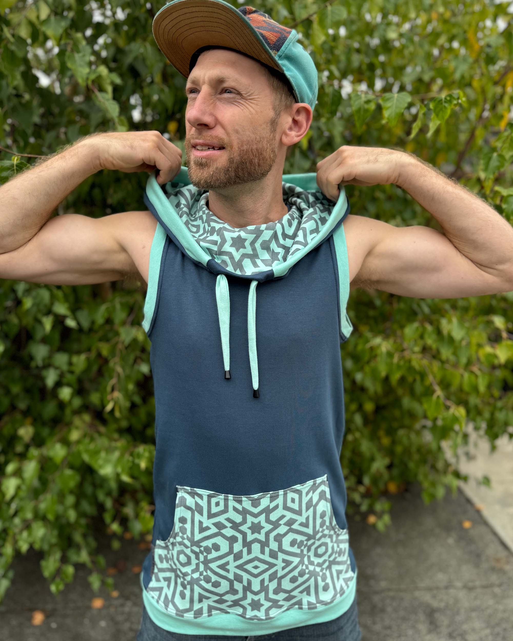 Organic cotton sleeveless hoodie, deep blue with mint geo print accents, front view on male model.