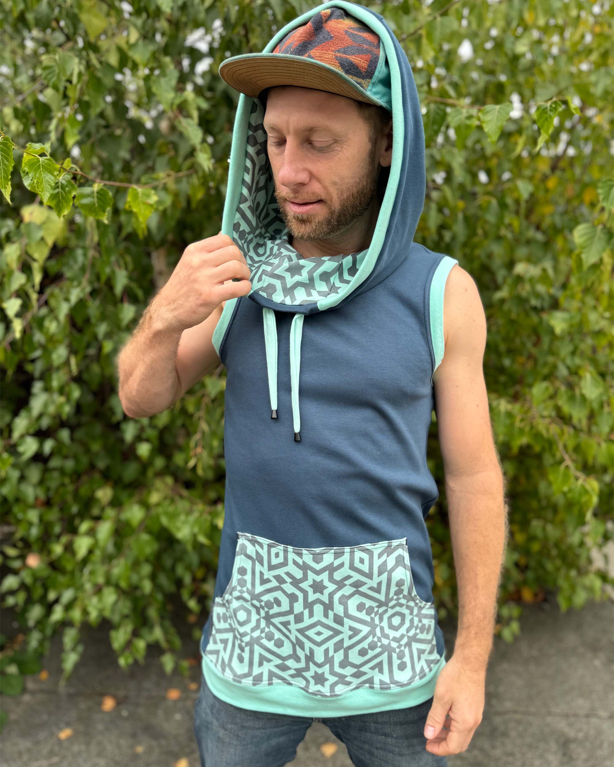 Organic cotton sleeveless hoodie, deep blue with mint colored geo print accents, front view on male model.