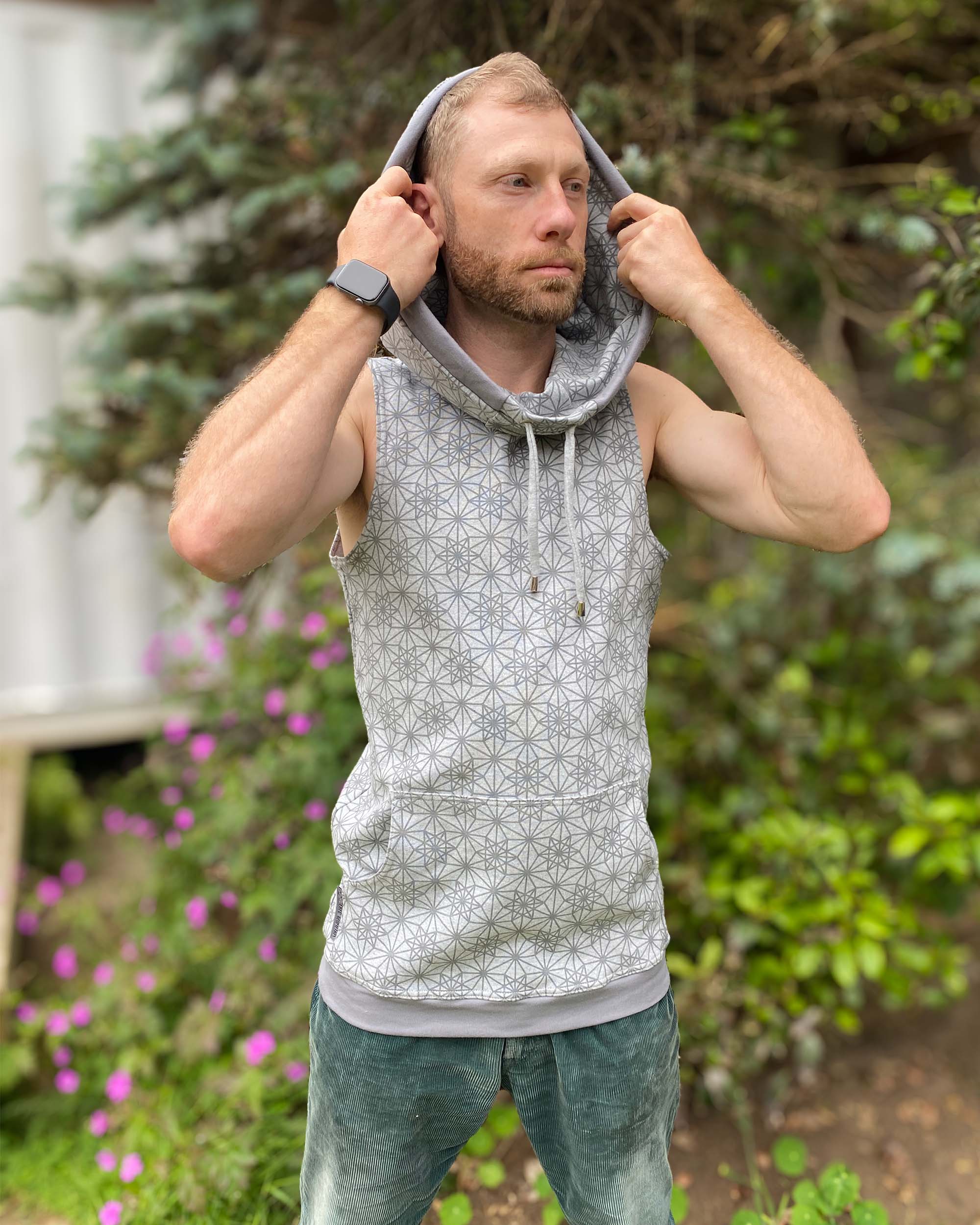 Organic cotton sleeveless hoodie, grey with geometric print, front view on male model, hood up.