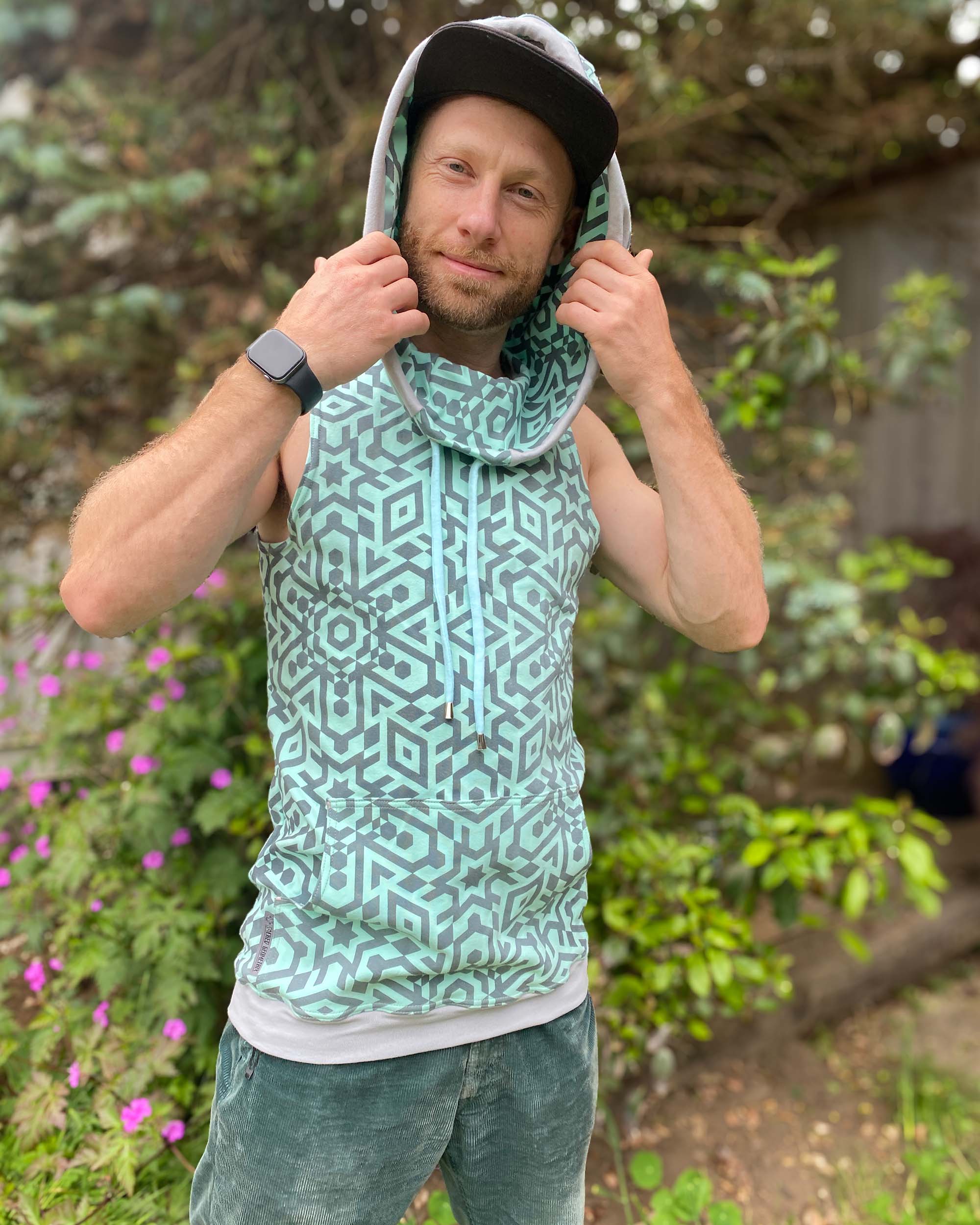 Organic cotton sleeveless hoodie, mint with geometric print fabric, front view on male model, hood up.