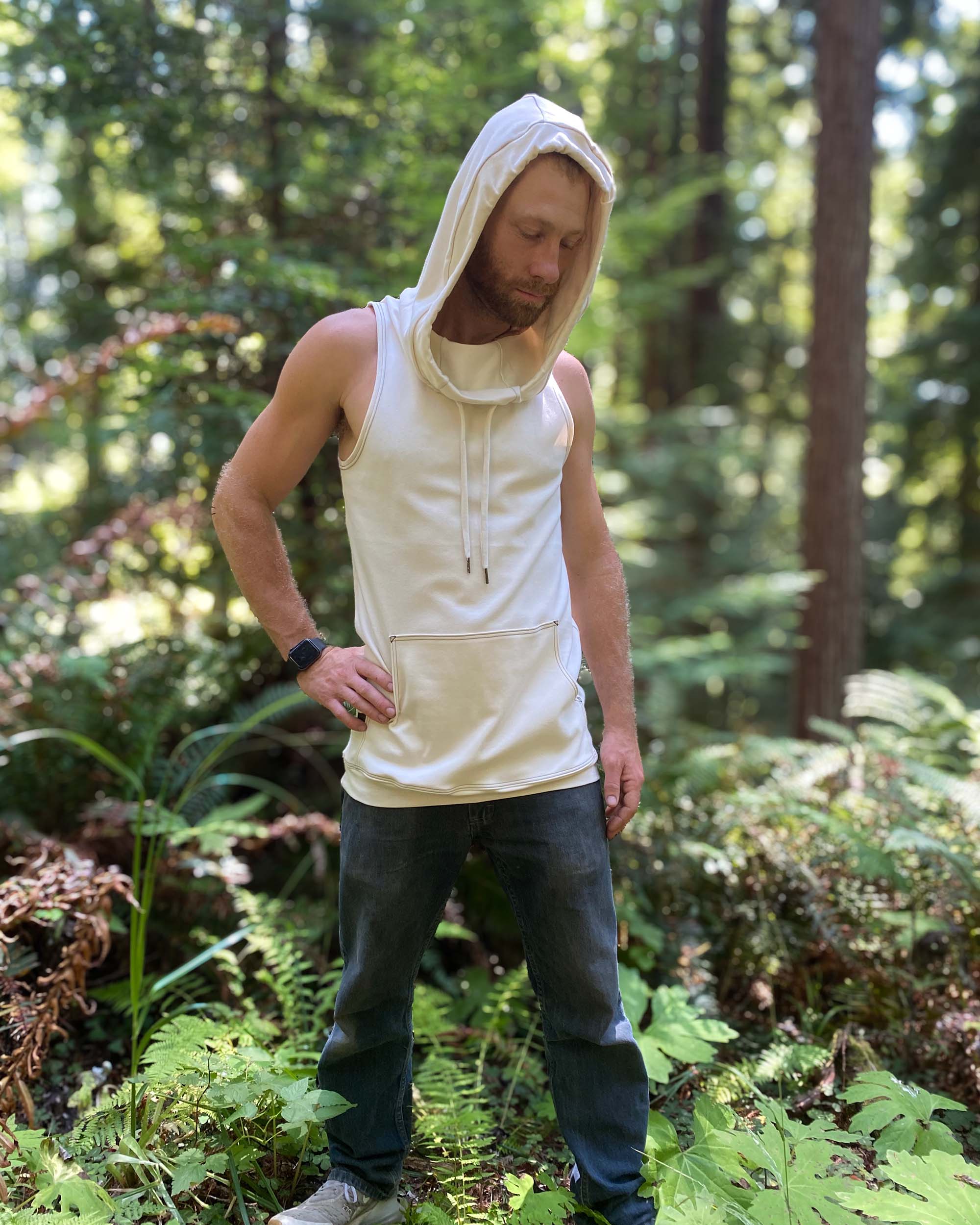 Organic cotton sleeveless hoodie, undyed fabric, front right side view on male model with hood up.
