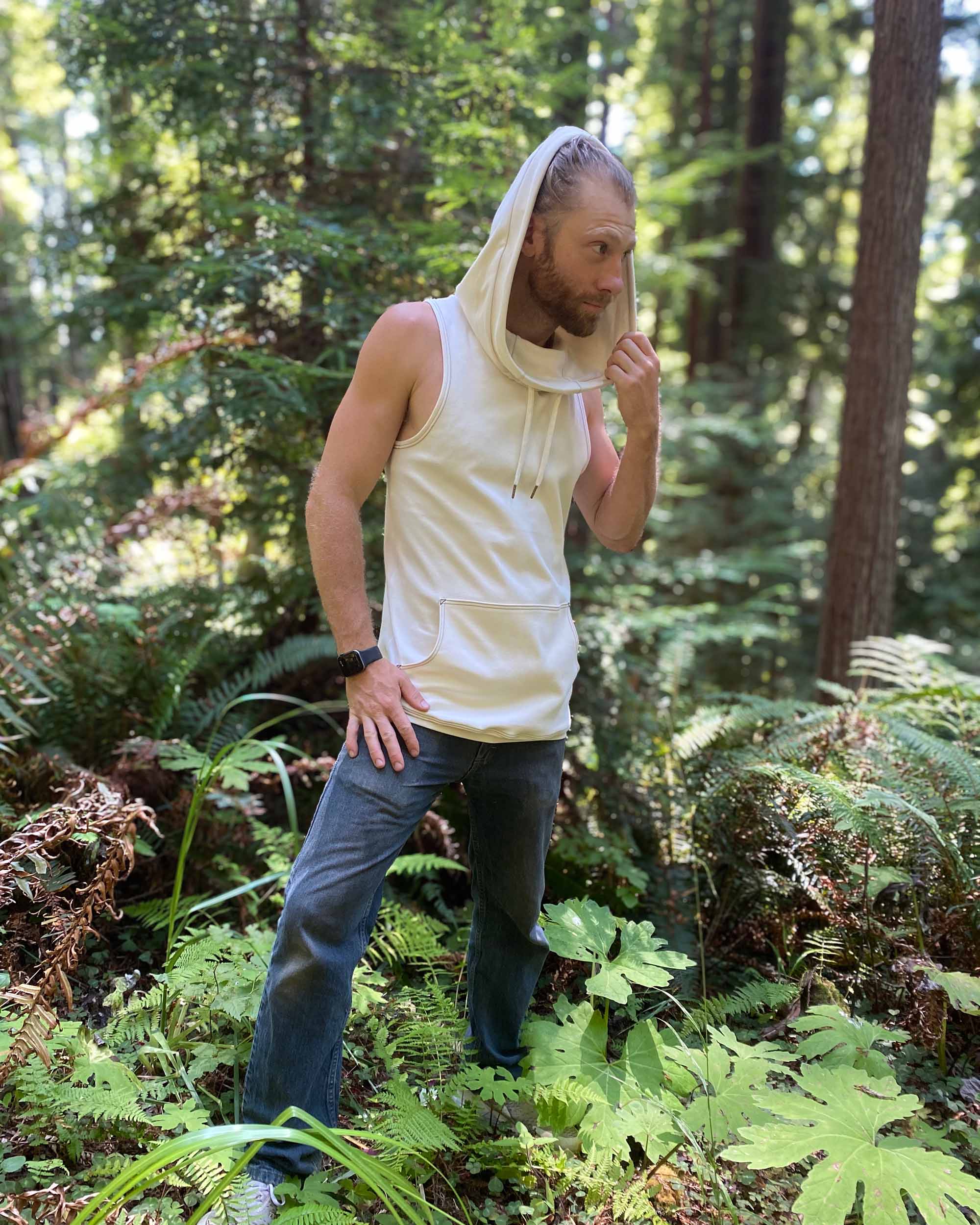 Organic cotton sleeveless hoodie, undyed fabric, front left side view on male model in nature.