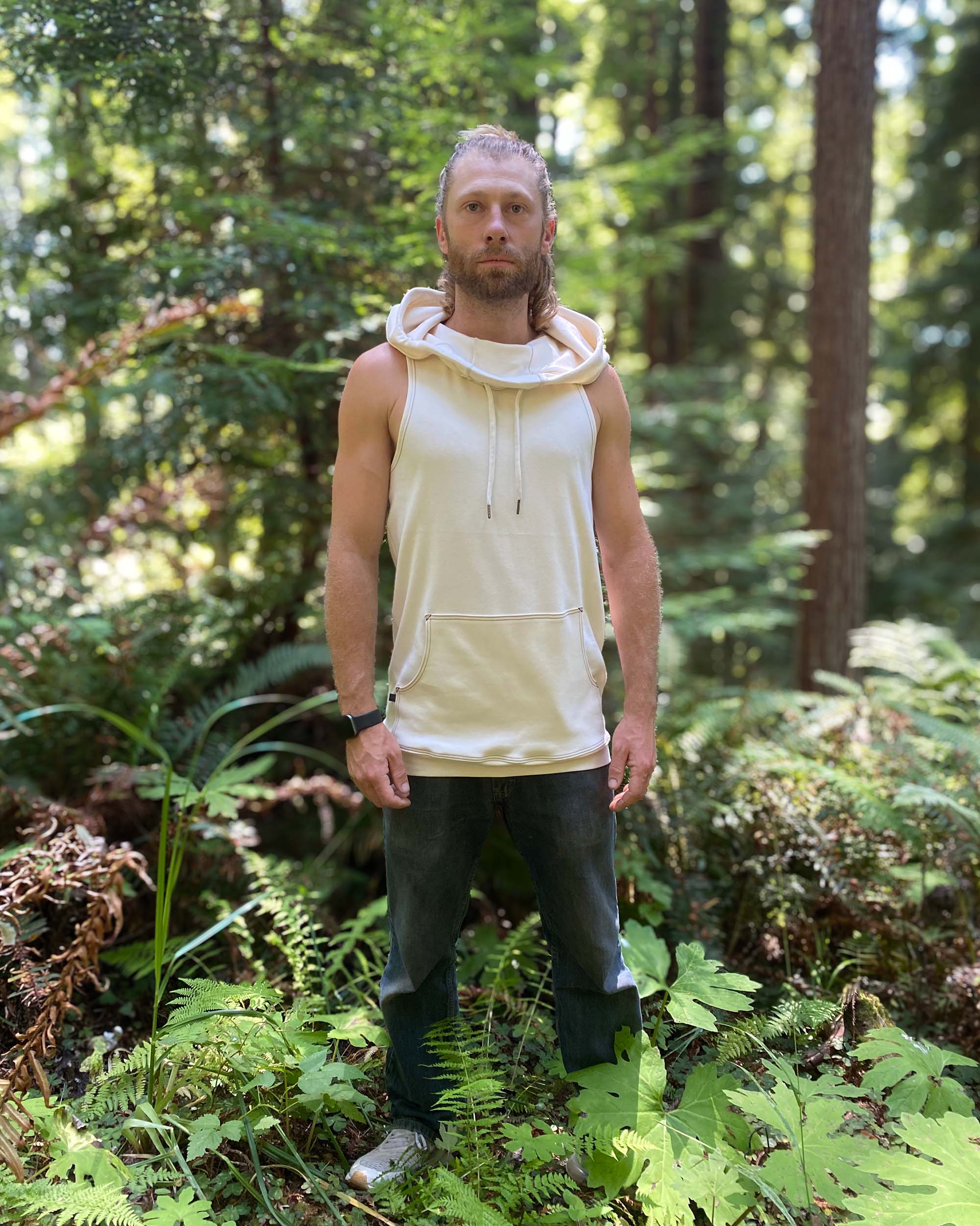 Organic cotton sleeveless hoodie, undyed fabric, front view on male model in nature.