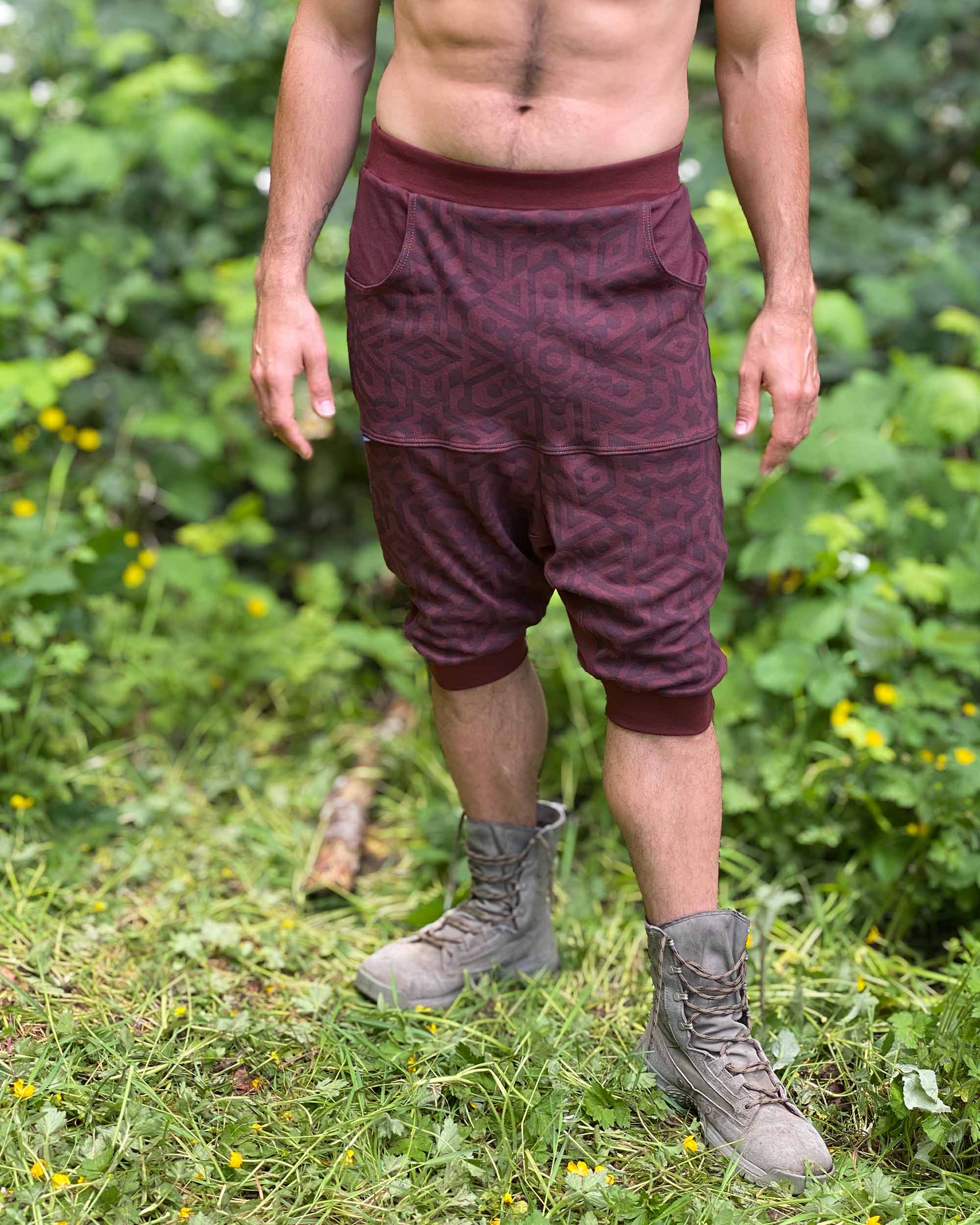 Organic cotton drop crotch shorts, brown fabric with geometric print, front view on male model in nature.