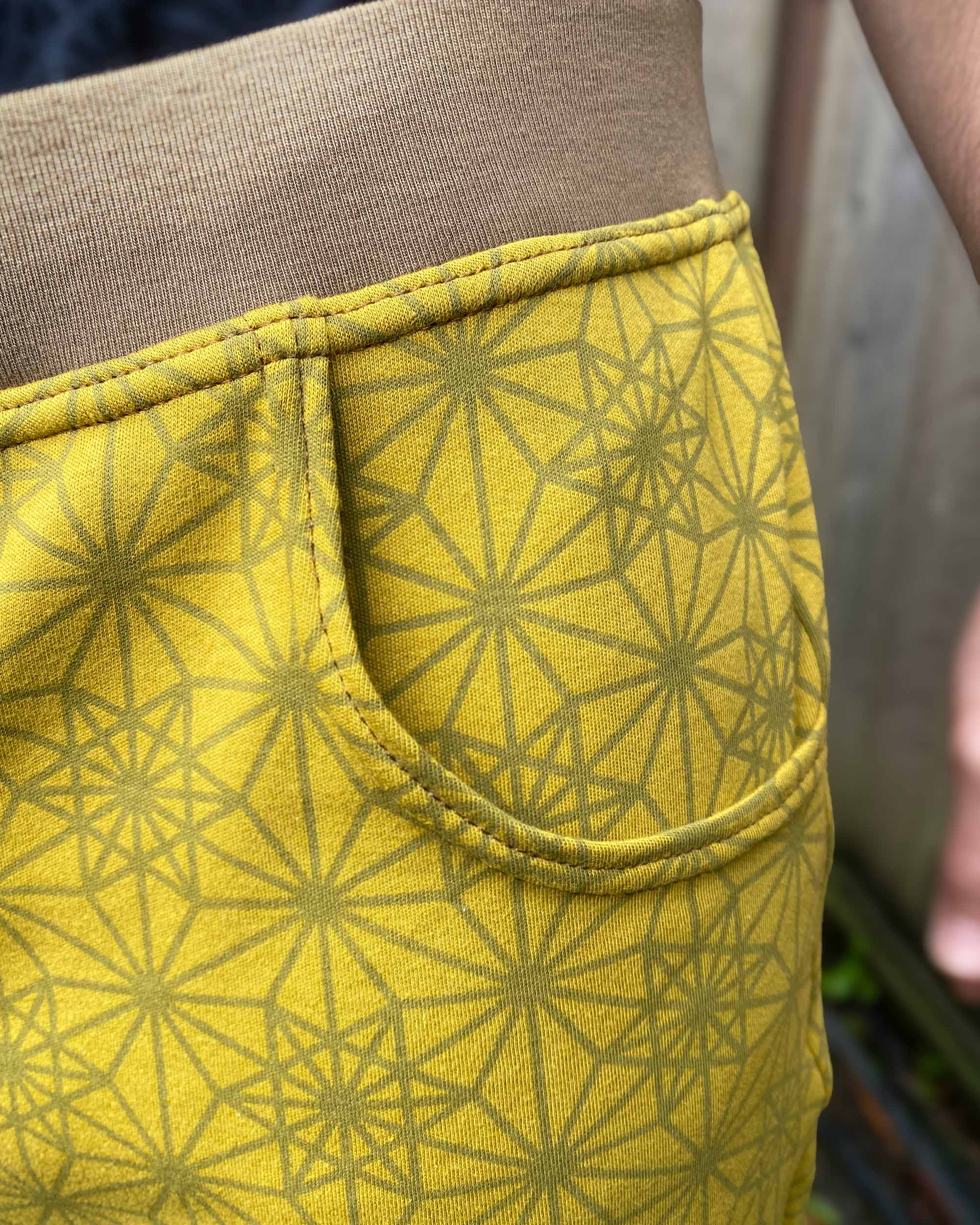 Organic cotton drop crotch shorts, yellow fabric with geometric print, detail view of pocket.
