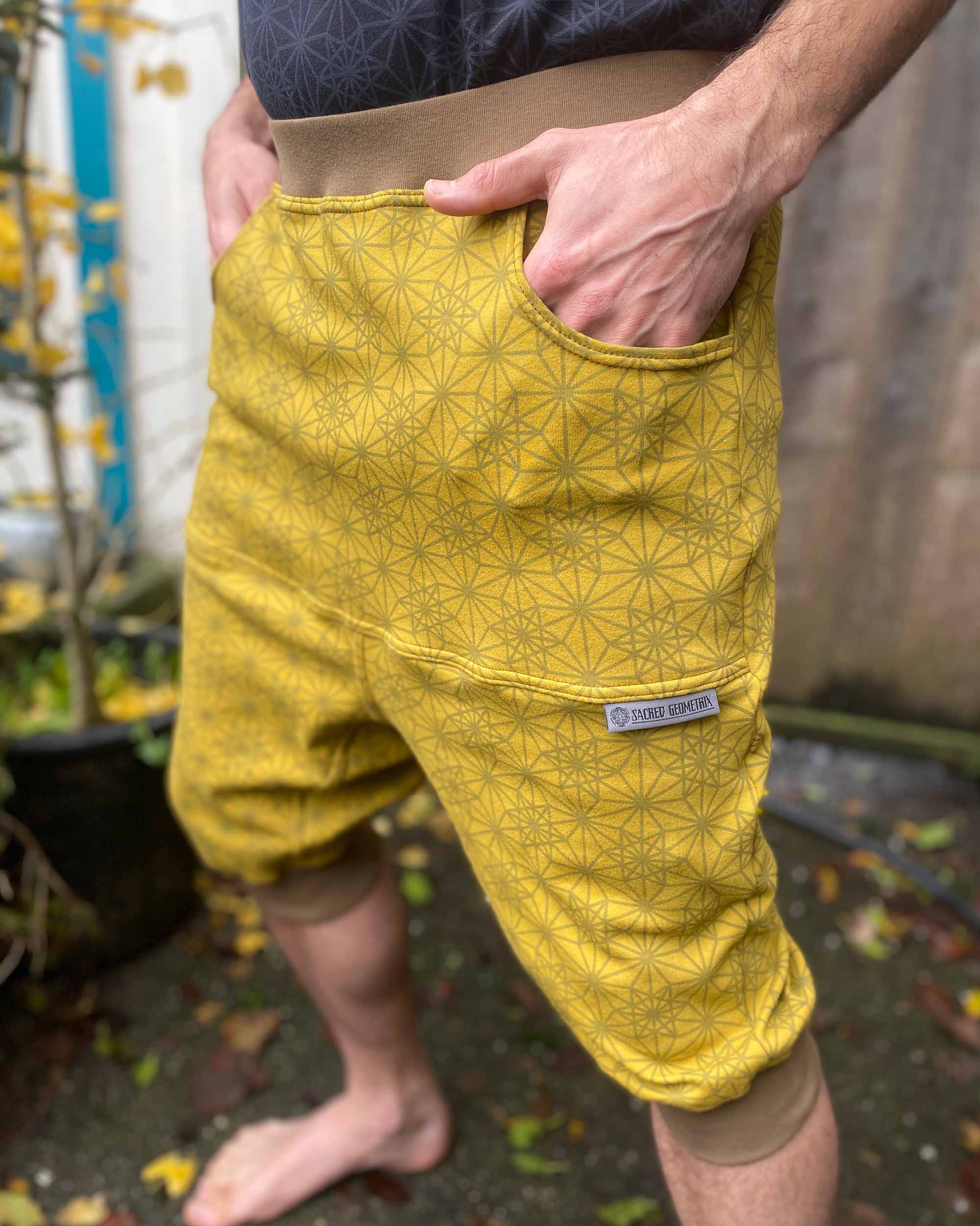 Organic cotton drop crotch shorts, yellow fabric with geometric print, front left side detail view on model.