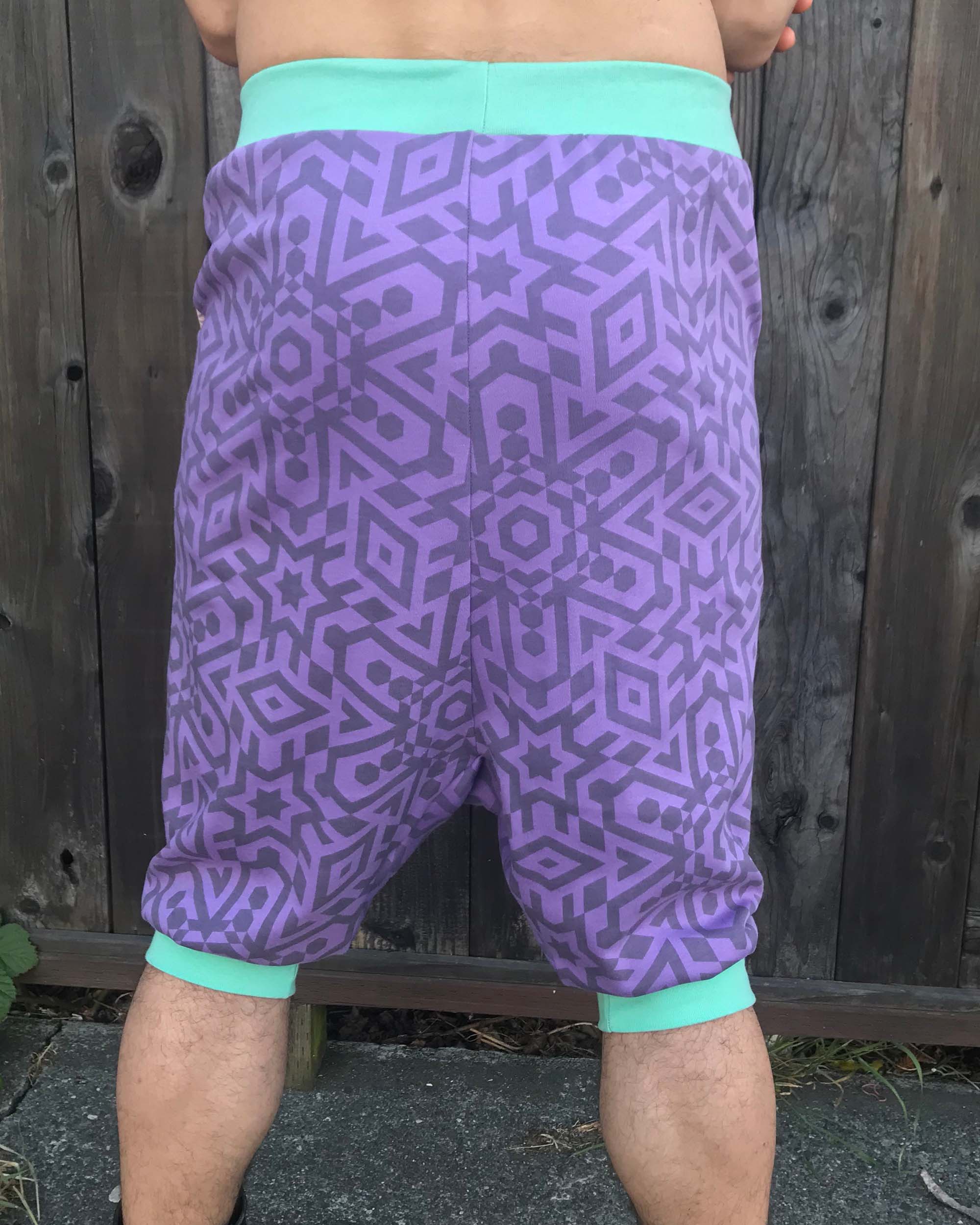 Organic cotton drop crotch shorts, lavender fabric with geometric print, back view on model.
