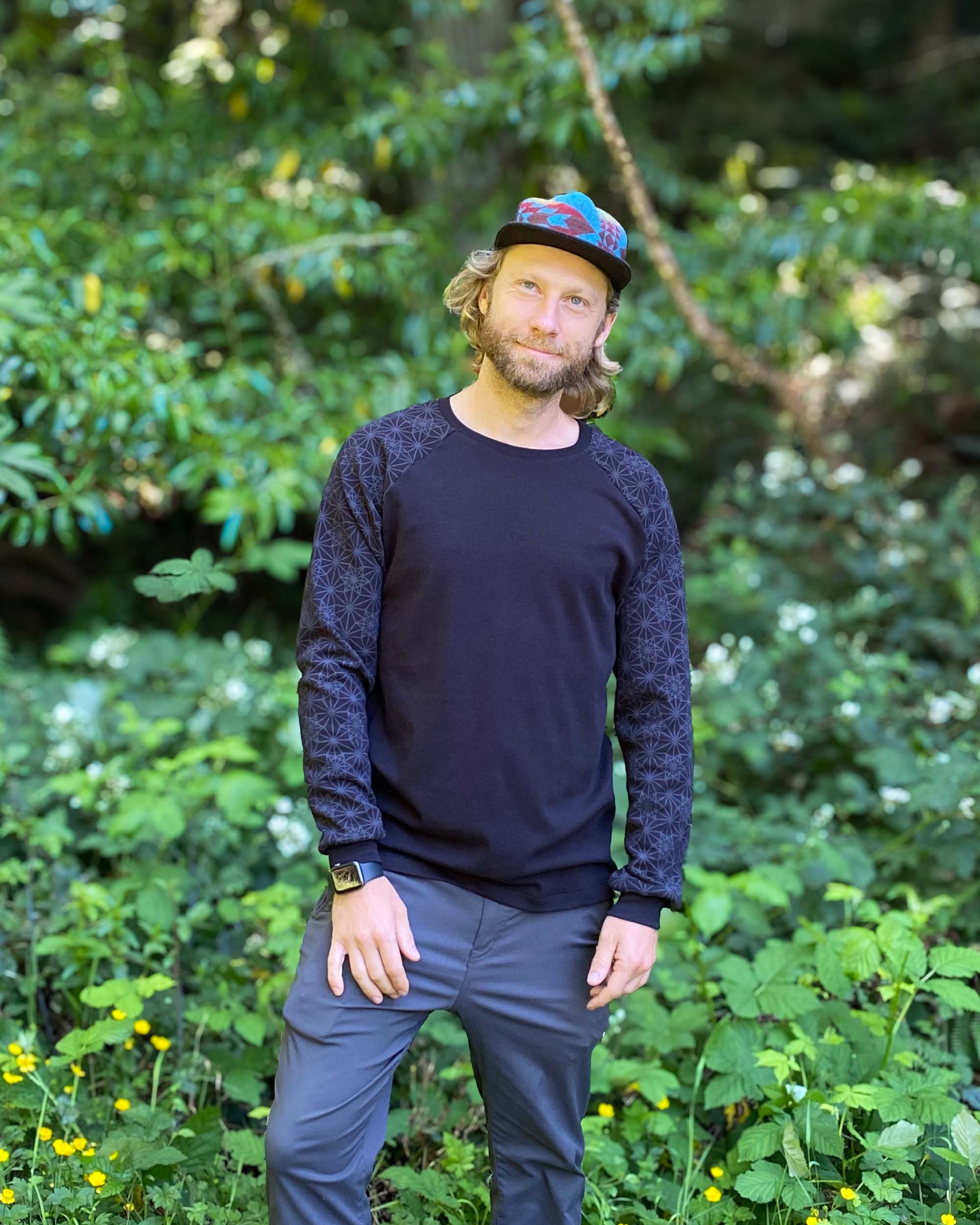 Organic cotton long sleeve shirt, black with geometric sleeve prints, front right view on male model in nature.