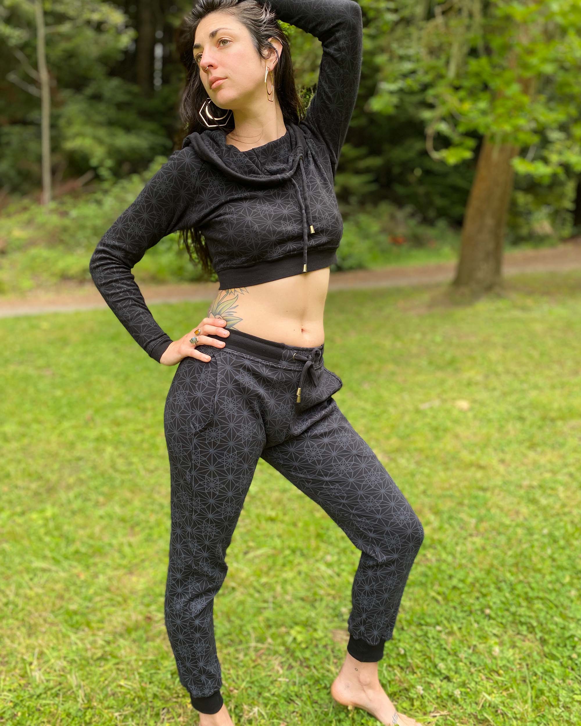 Organic cotton unisex joggers, black fabric with geometric print, full body front view on female model in nature.
