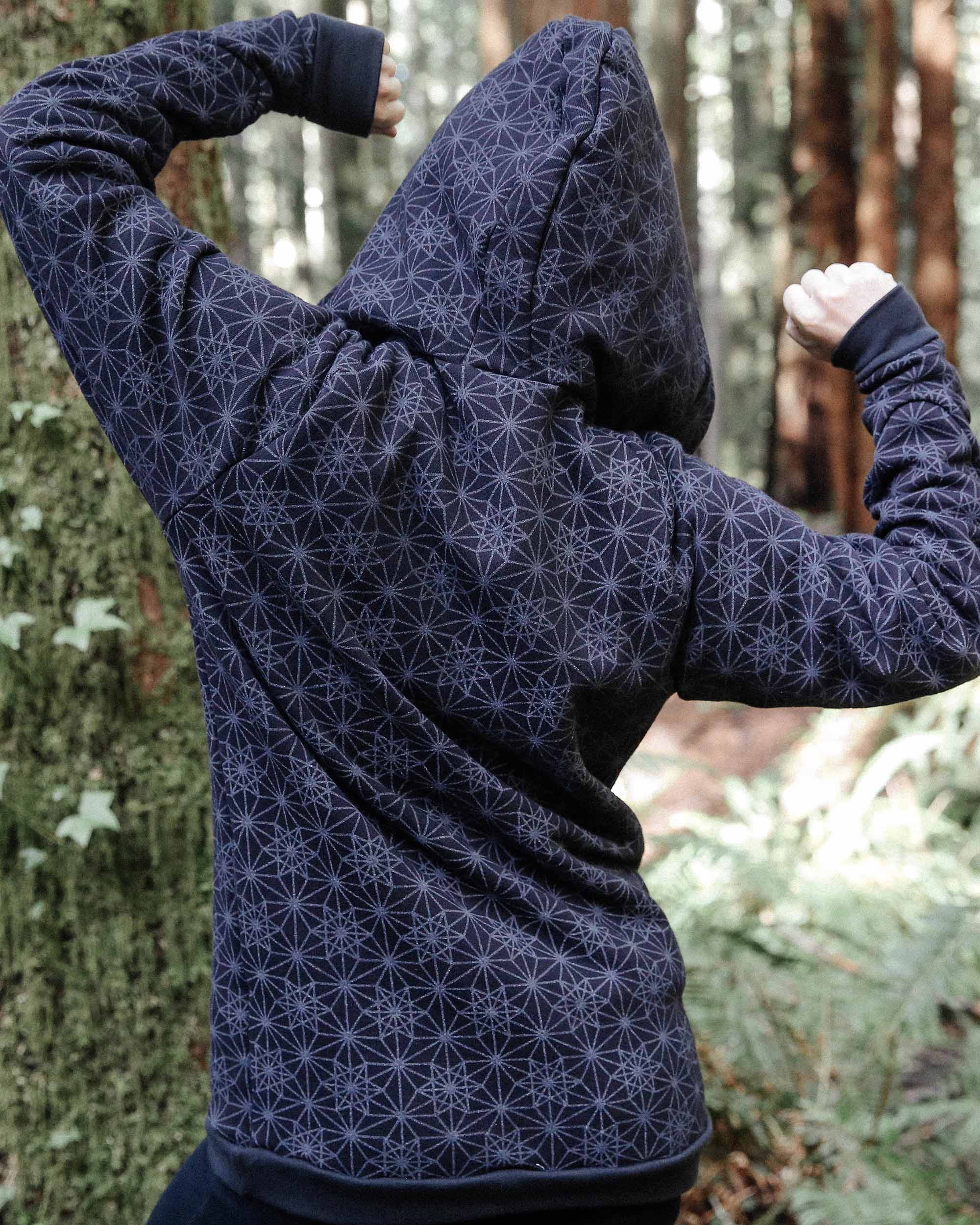 Organic cotton fleece unisex hoodie, black fabric with geometric print, back side view on female model in nature.
