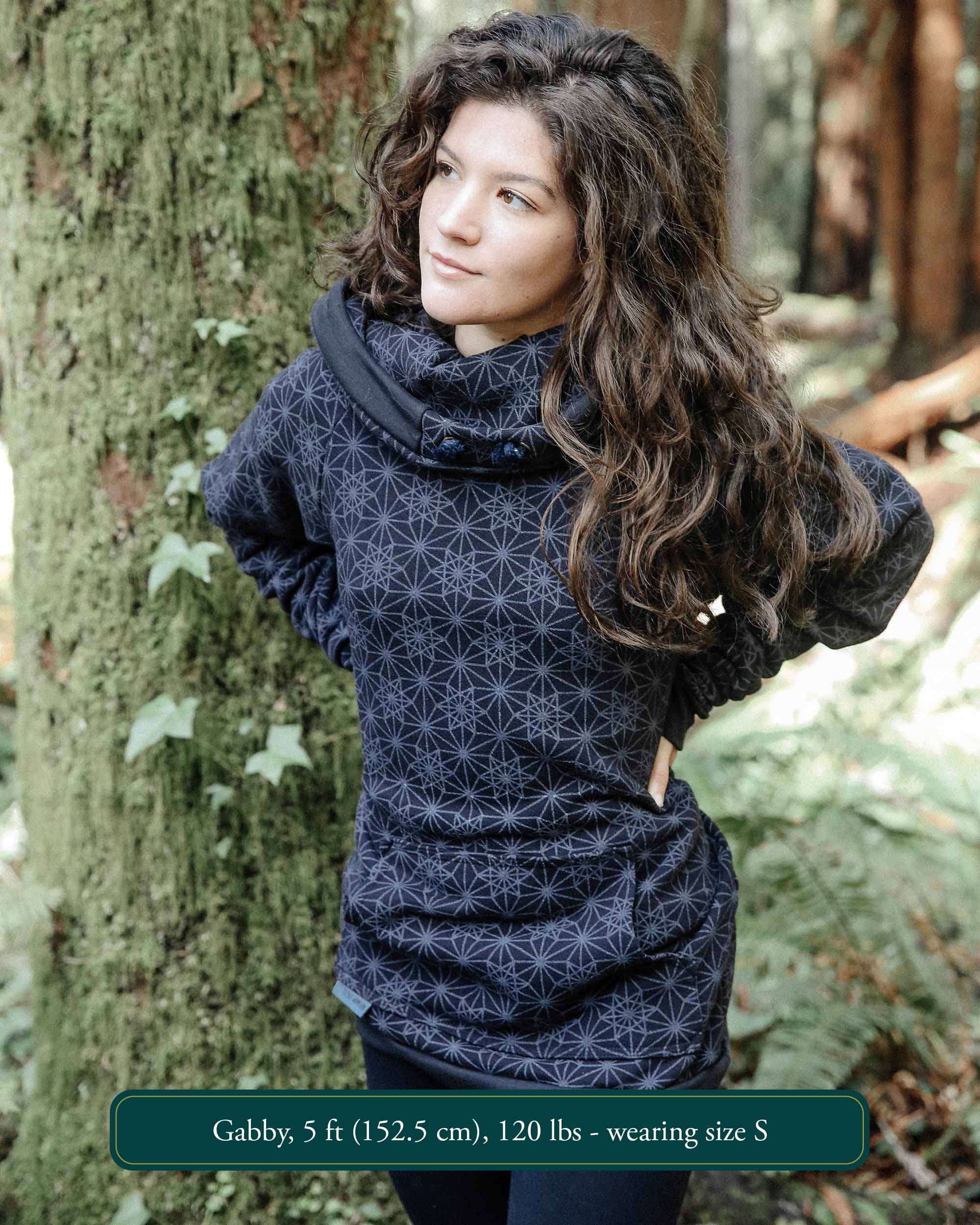 Organic cotton fleece unisex hoodie, black fabric with geometric print, front left view on female model in nature.
