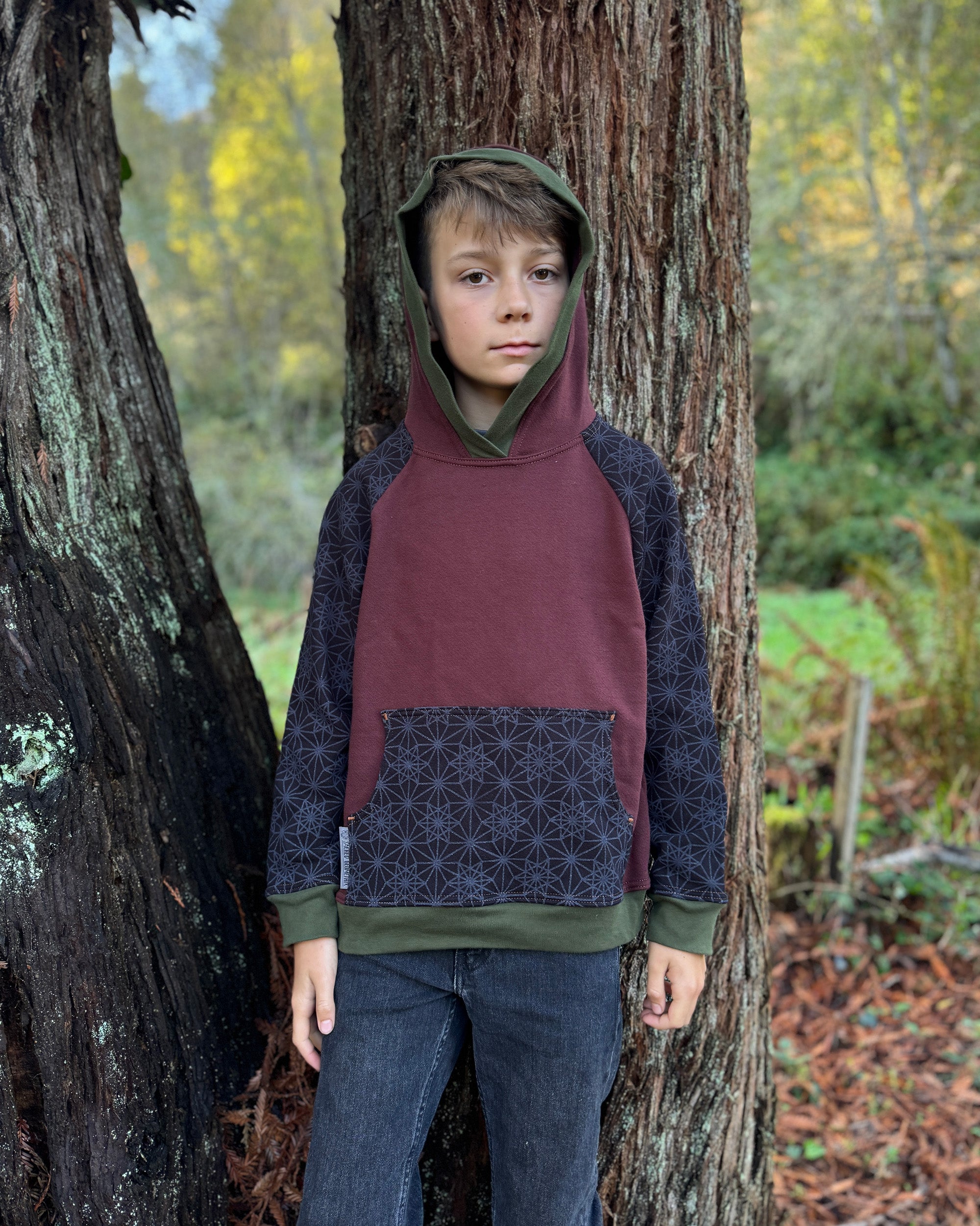 Fleece youth hoodie, black fabric with geometric print, front view on boy model with trees.