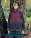 Organic cotton fleece kids hoodie, black fabric with geometric print, front view on boy model in nature.