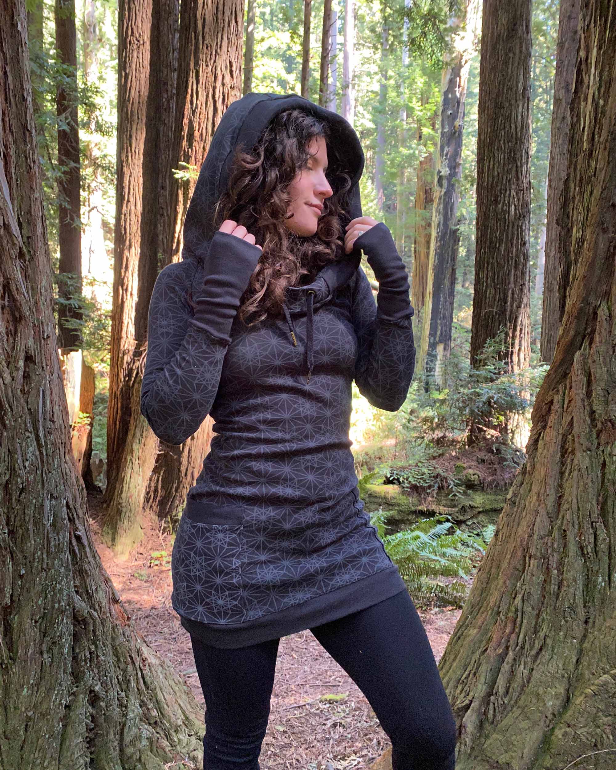 Organic cotton hooded long sleeve dress, black with geometric print, front view on female model in redwoods.