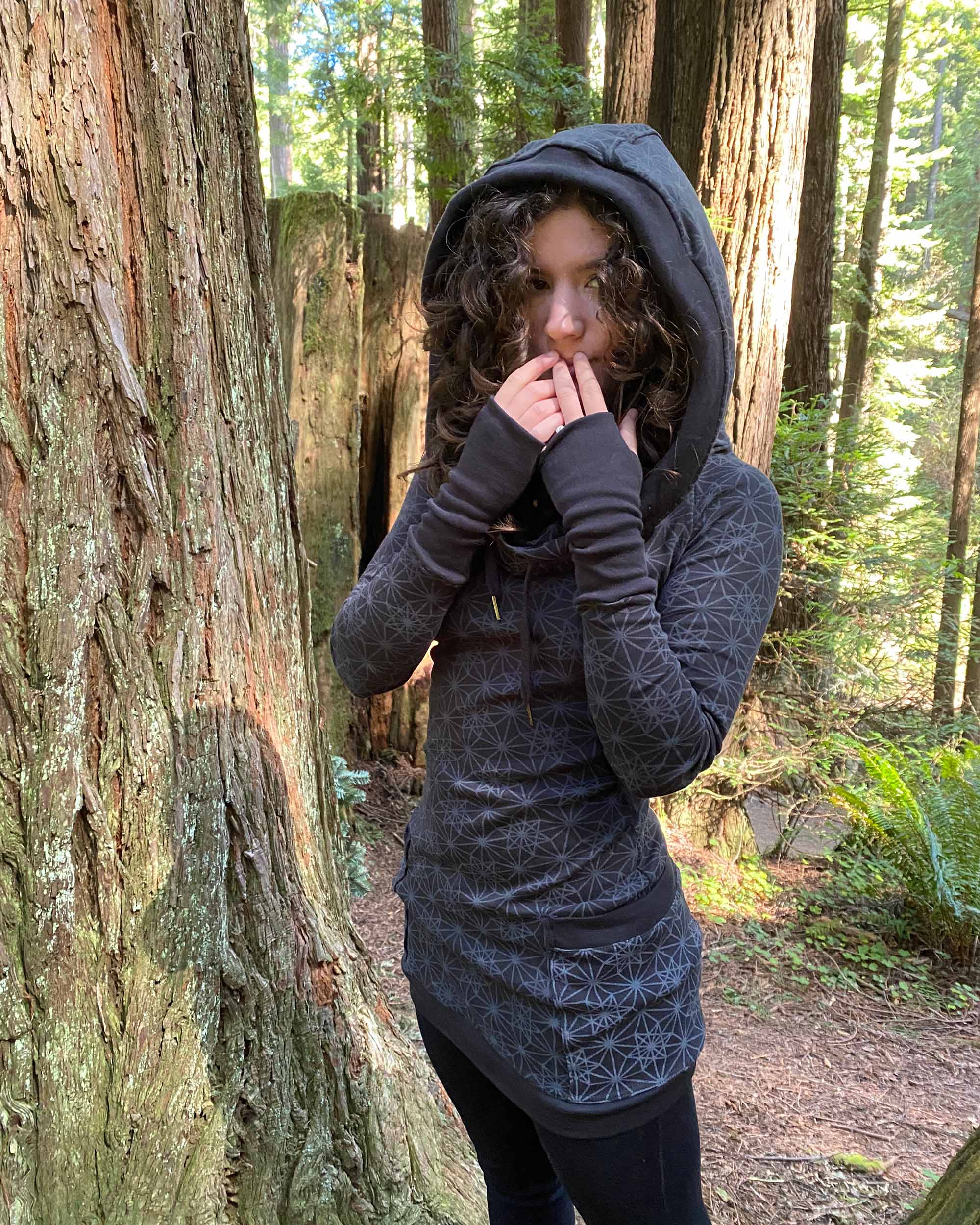 Organic cotton hooded long sleeve dress, black with geometric print, front view on female model, hood up.