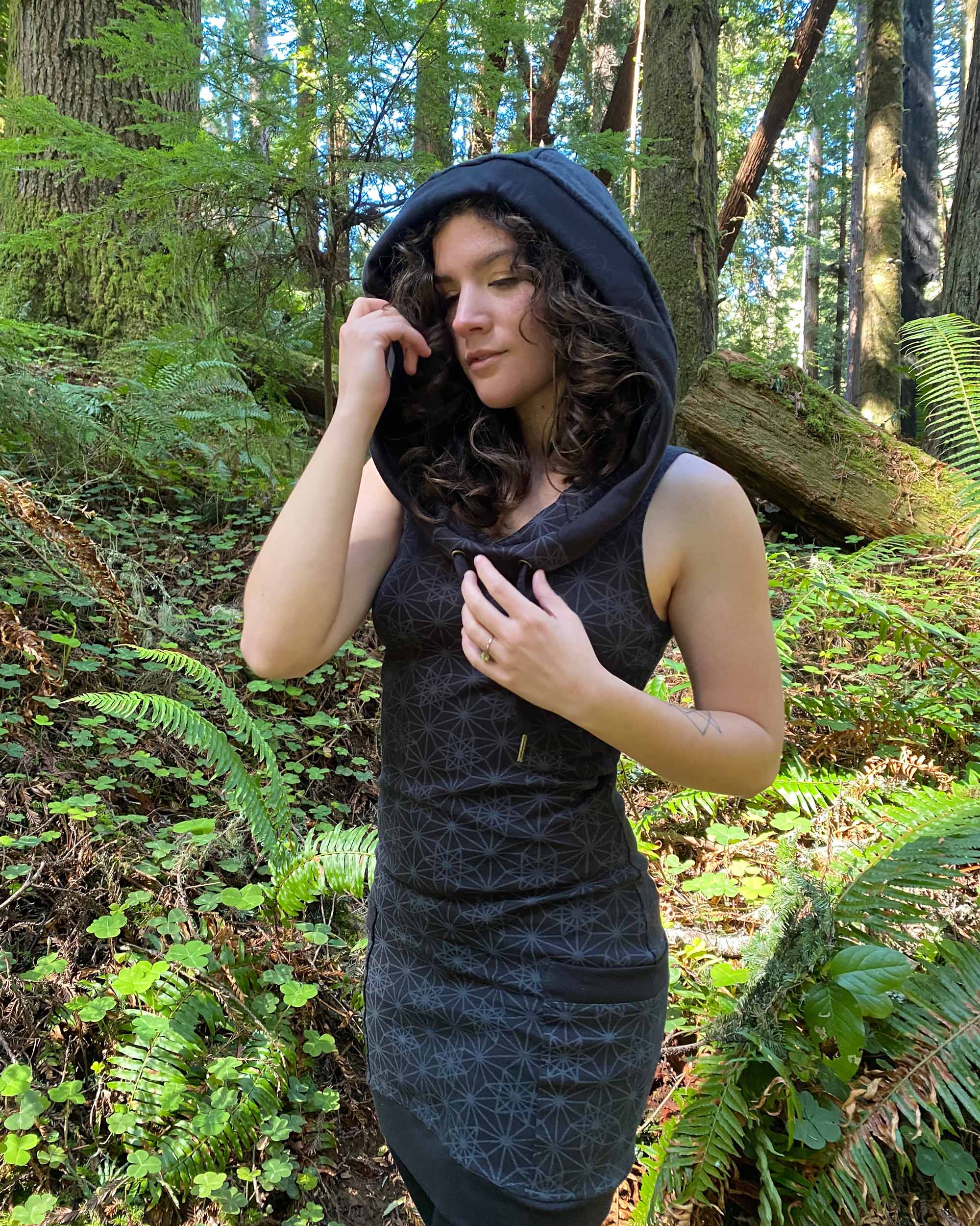 Organic cotton sleeveless hooded dress, black fabric with geo print, front left side view on female model.