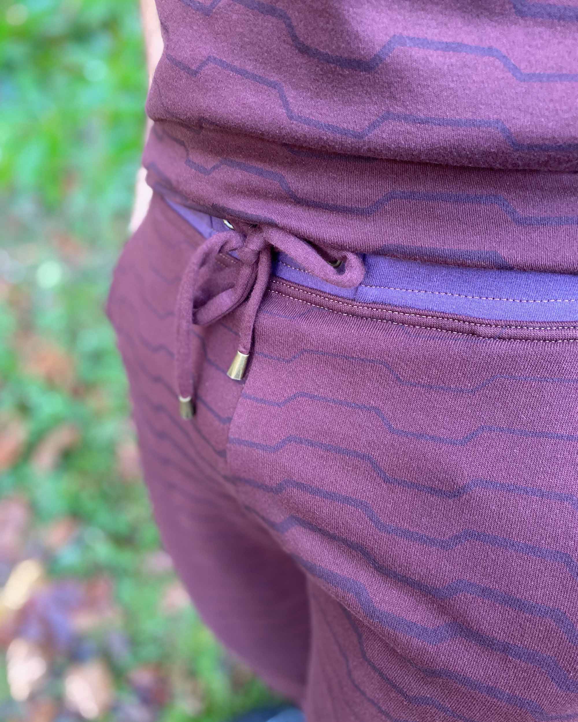 Organic cotton fleece joggers, reddish brown fabric with geometric all over print, detail front view of drawcord.