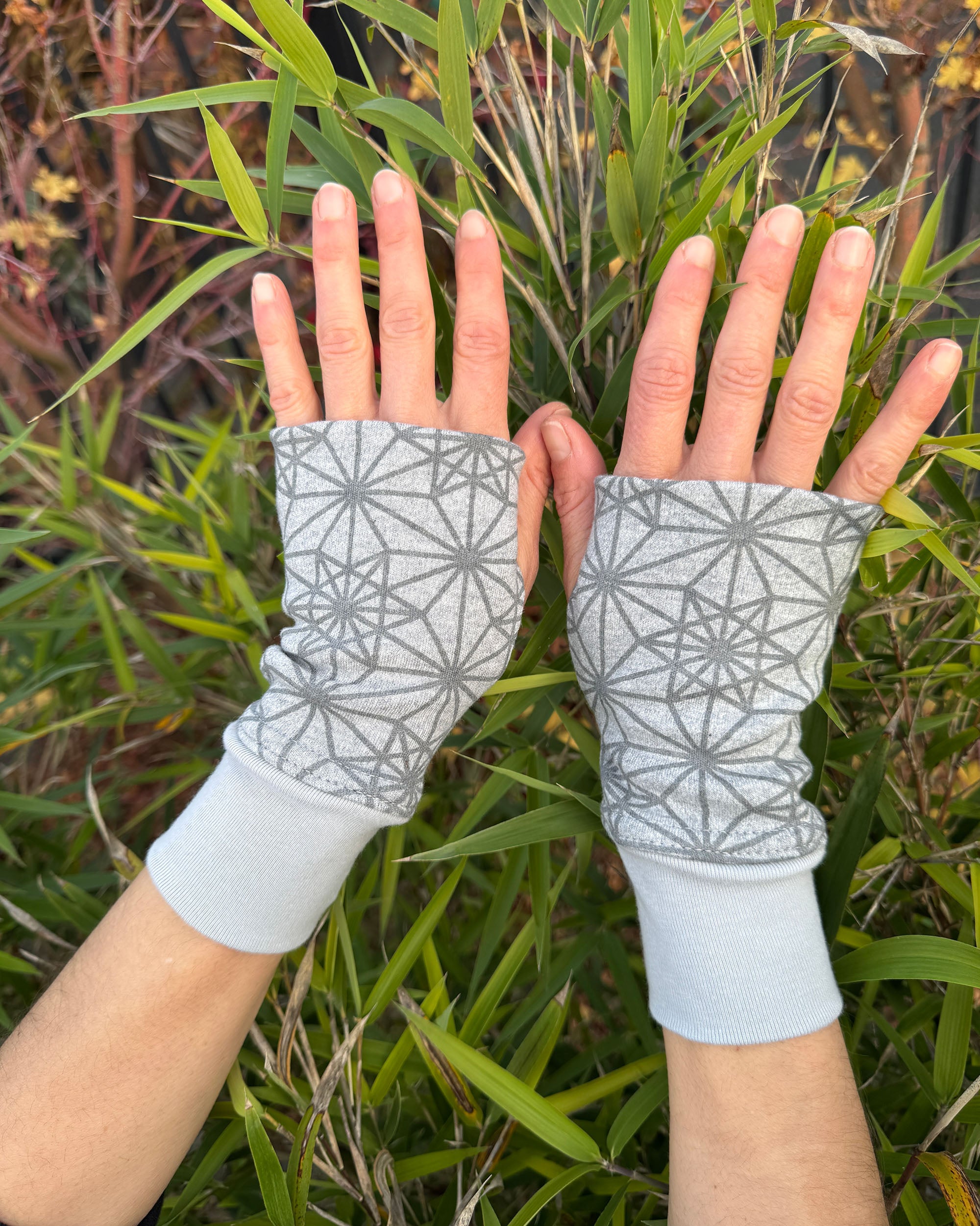 Hands wearing organic cotton hand warmers, grey colored geometric fabric with nature background.