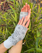 Hands wearing grey colored geometric organic cotton hand warmers, with nature background.