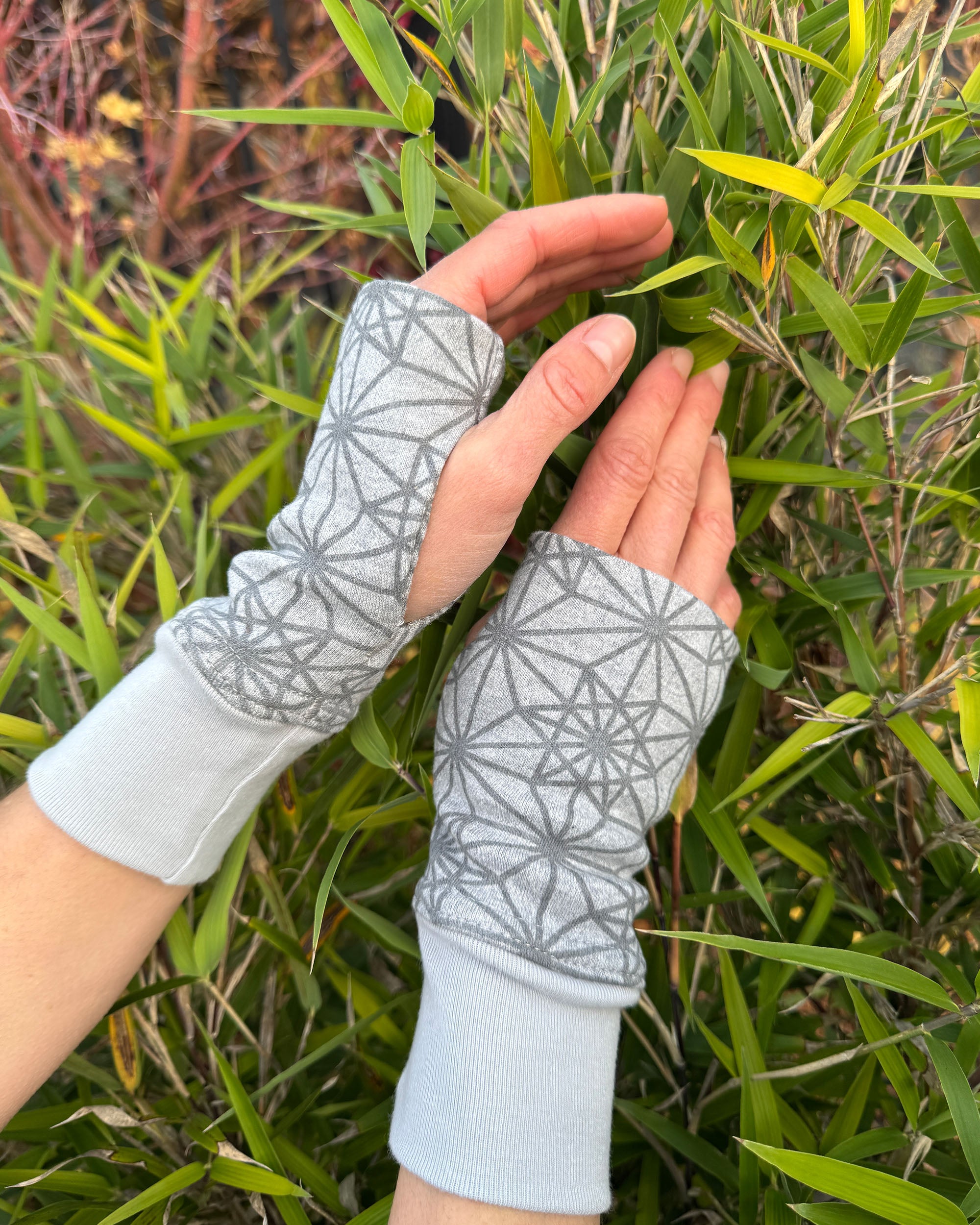 Female hands wearing grey colored geometric organic cotton hand warmers, with nature background.