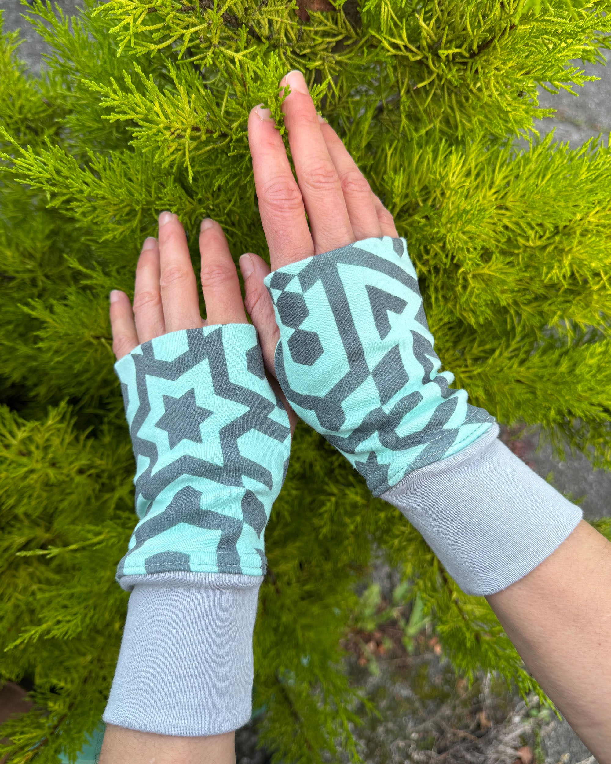 Female hands wearing organic cotton hand warmers, mint fabric with geometric print.