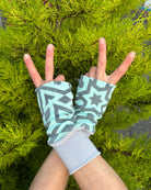 Female hands wearing organic cotton hand warmers, mint geometric fabric with natural background.